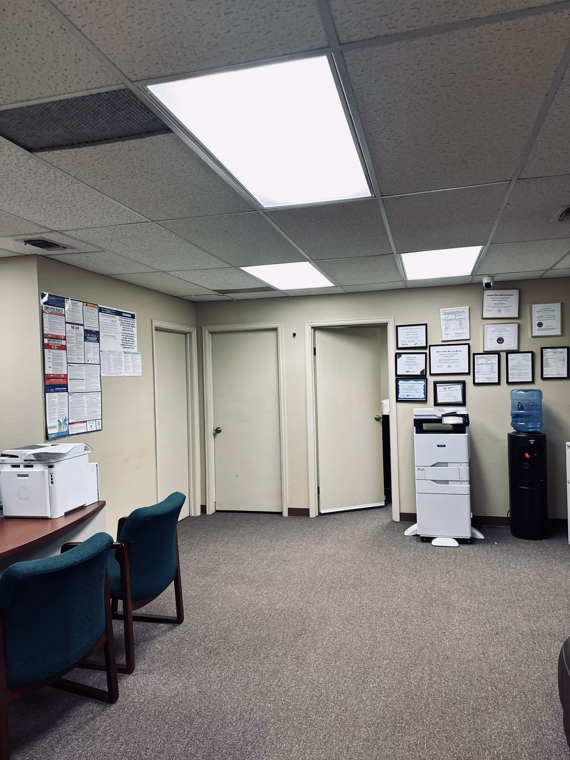 Office-like room with chairs, printer, water cooler, and framed certificates on walls.