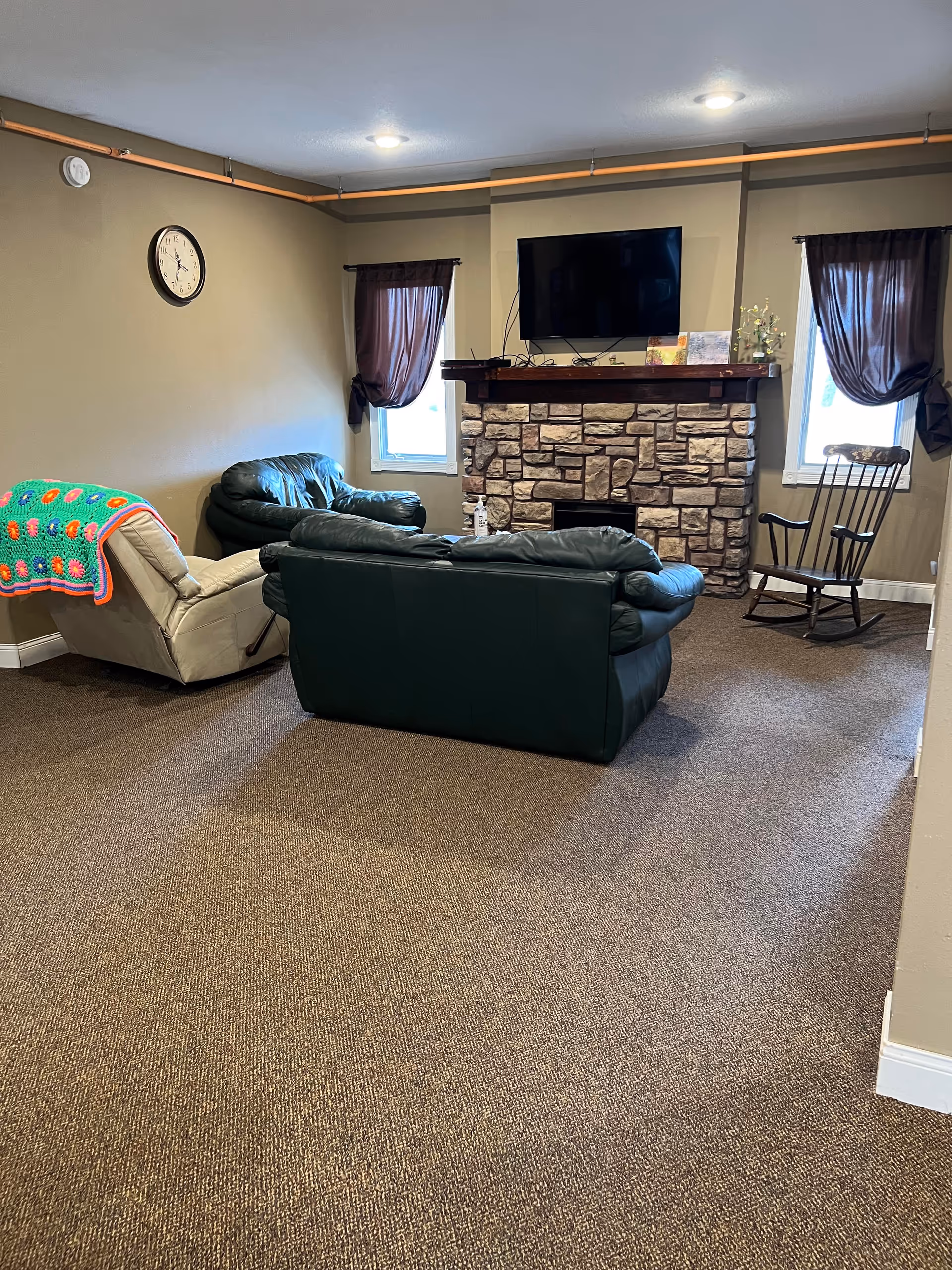 Cozy living room in a senior facility with a stone fireplace, TV, and seating.