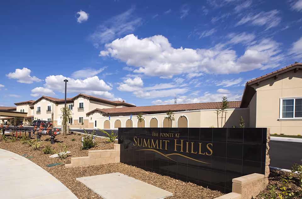 Exterior view of The Pointe at Summit Hills with a black sign and tan buildings.