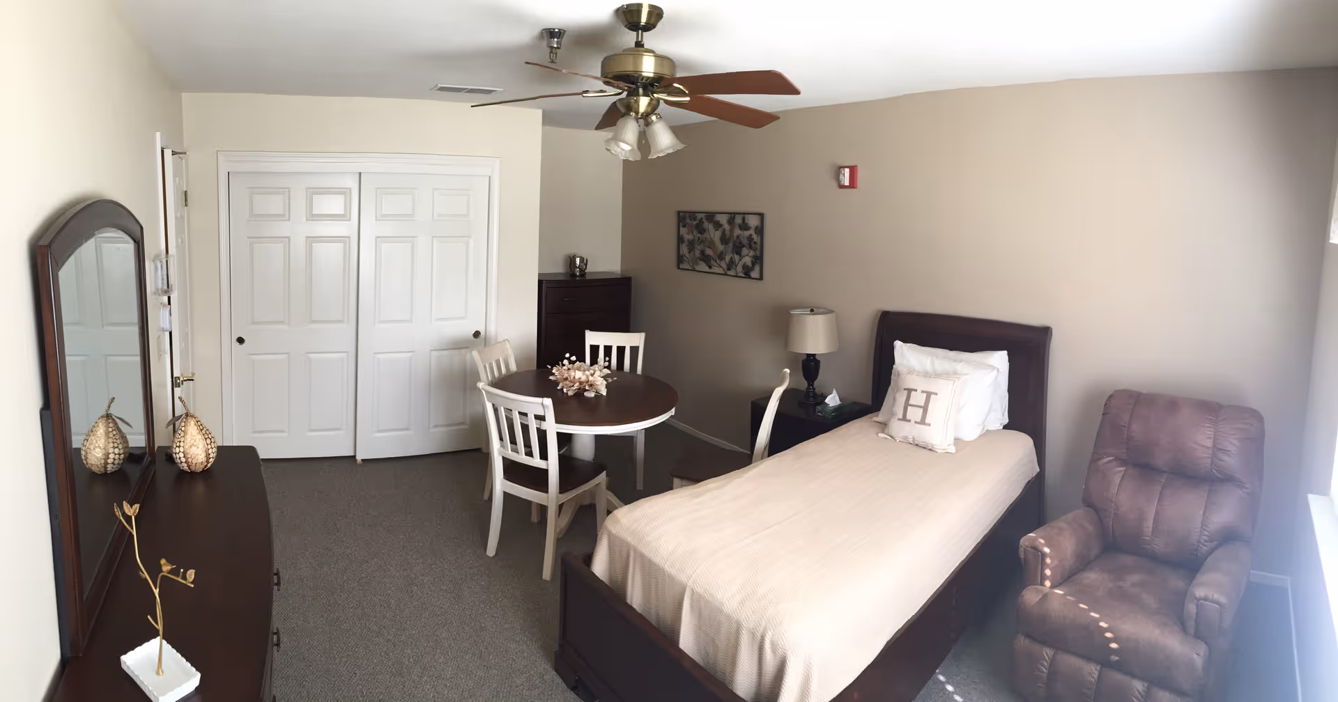 A furnished bedroom in Harvest at Fowler featuring bed, dresser, table, and chairs.