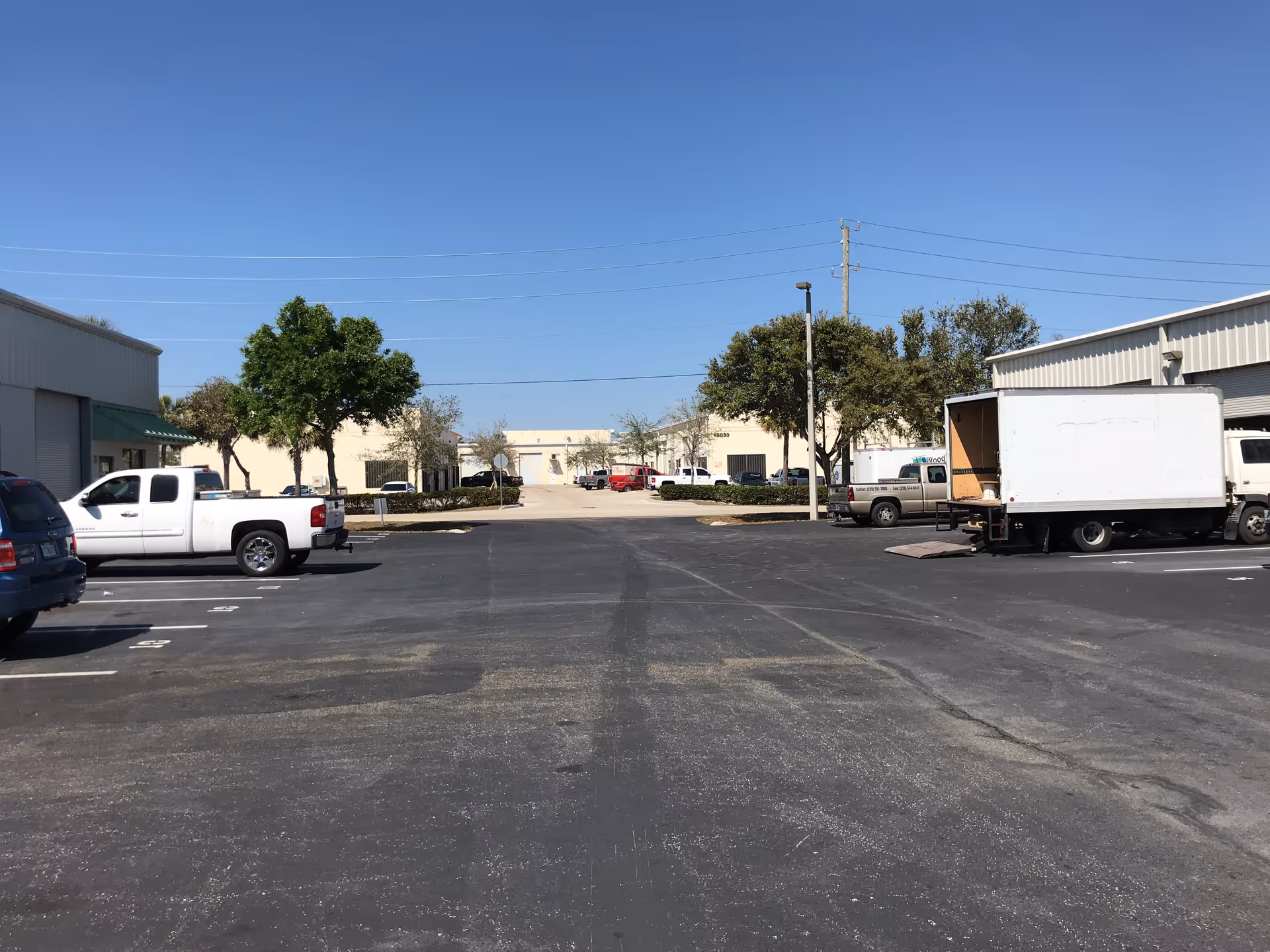 A wide parking lot in front of light industrial buildings with parked trucks.