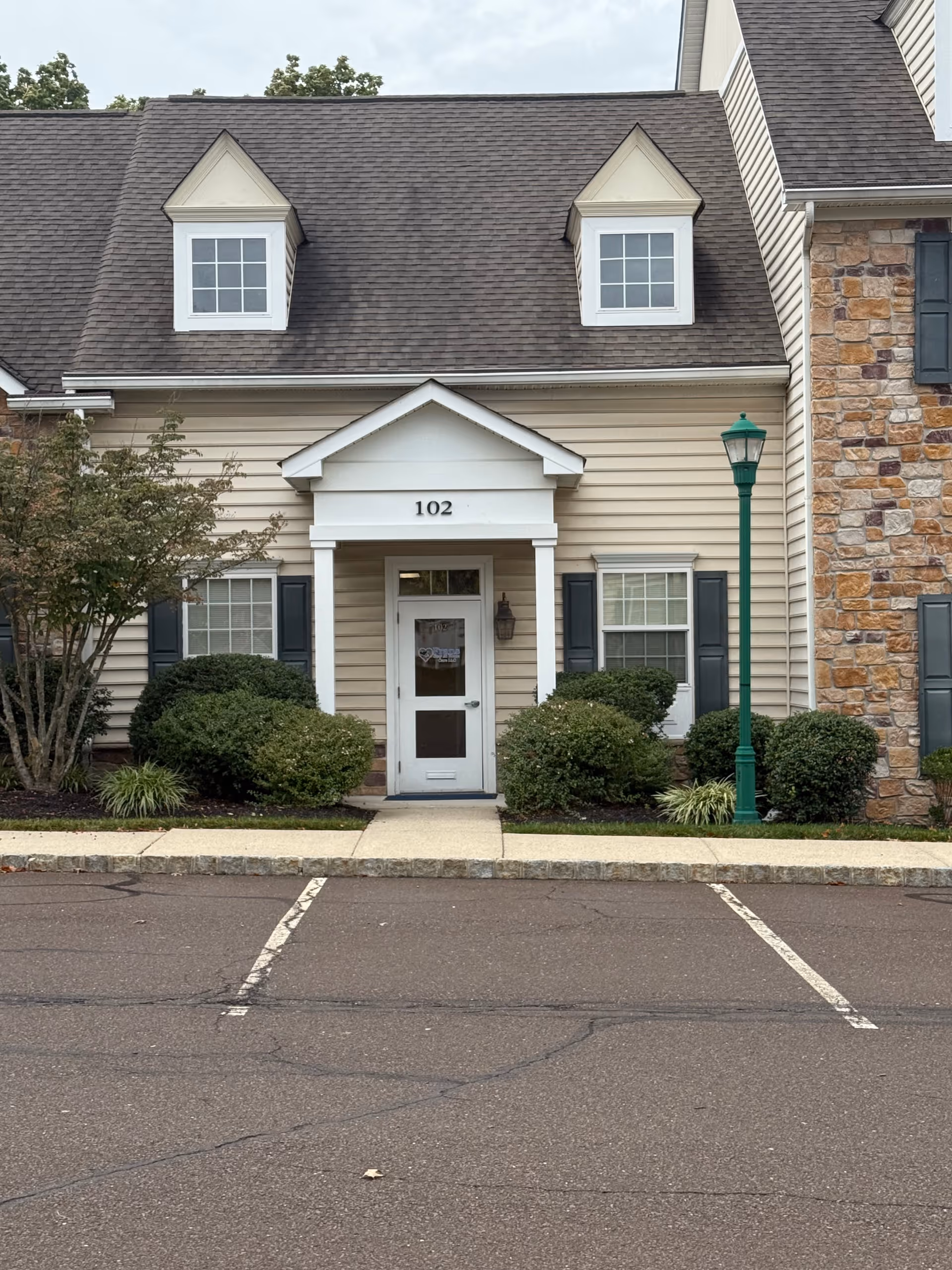 Front entrance of a townhouse-style building labeled 102 with shrubs and a green lamppost.