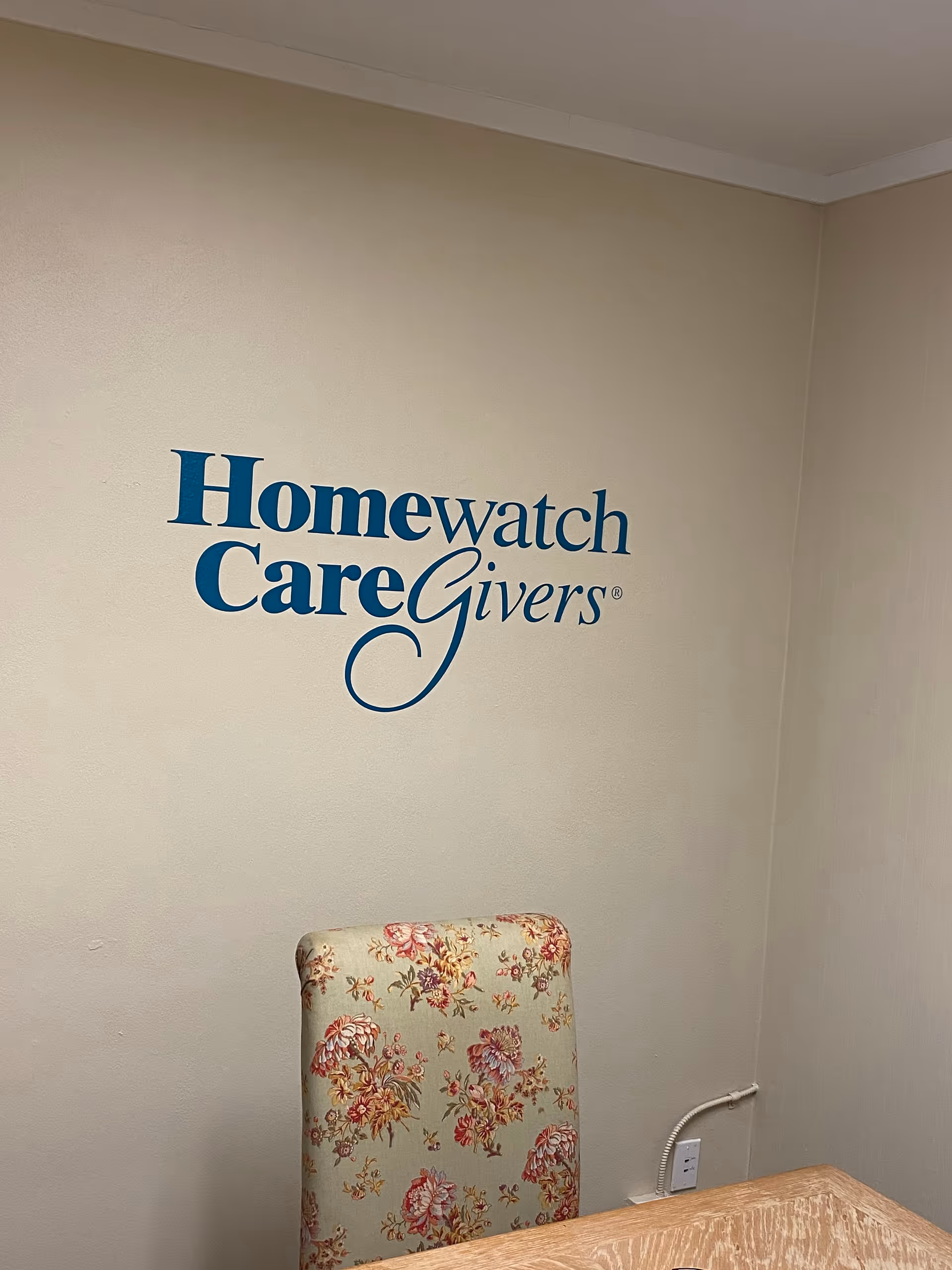 Interior wall displaying Homewatch CareGivers logo and a floral upholstered chair.
