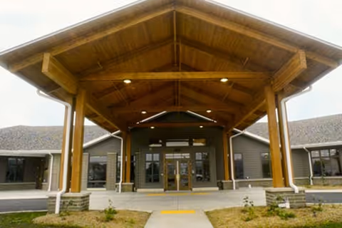 Wood-framed covered entrance to a senior living facility with glass doors.