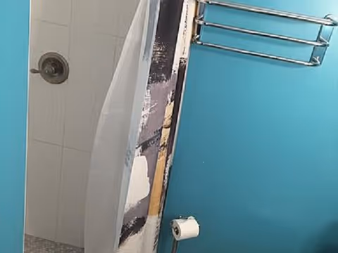 Blue bathroom with a shower curtain, tiled shower, towel rack, and toilet paper roll.