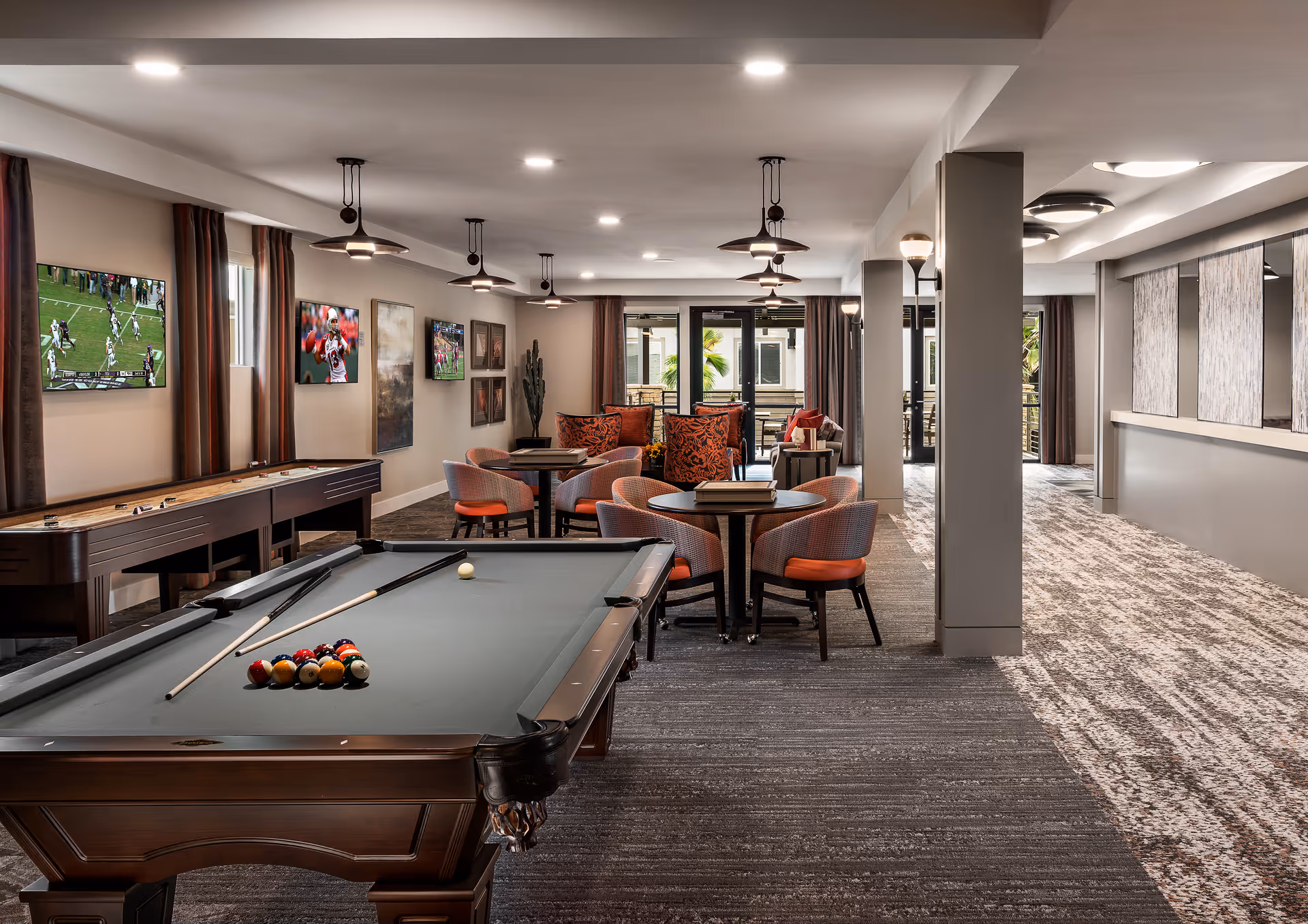 Open recreation room with a pool table, shuffleboard table, multiple seating areas, and wall-mounted TVs.