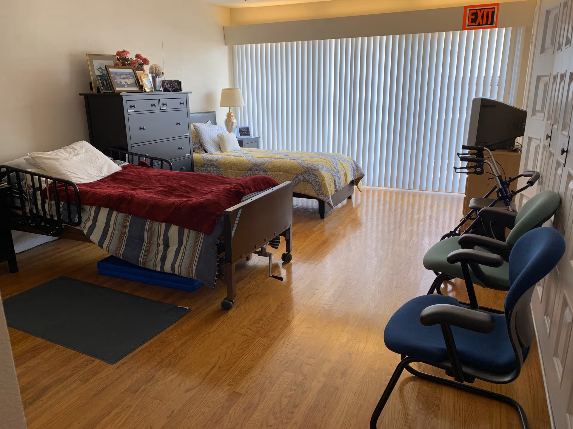A two-bed hospital-style bedroom with dresser, chairs, and a TV in a bright room.