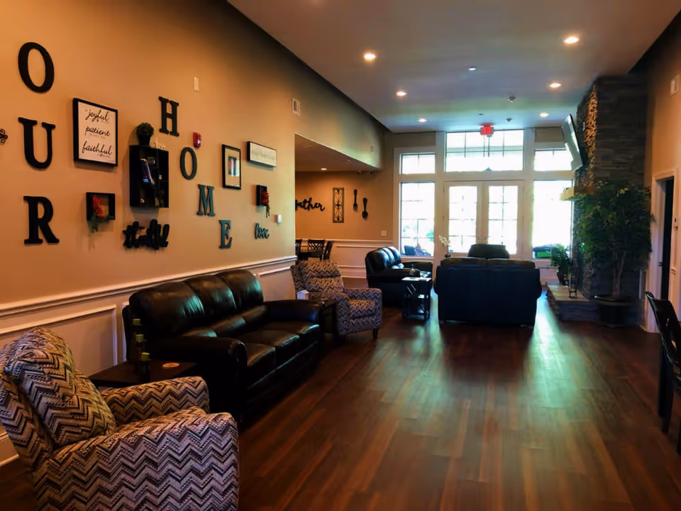 Cozy senior living lounge with leather sofas, patterned chairs, wall art, and bright back entry.
