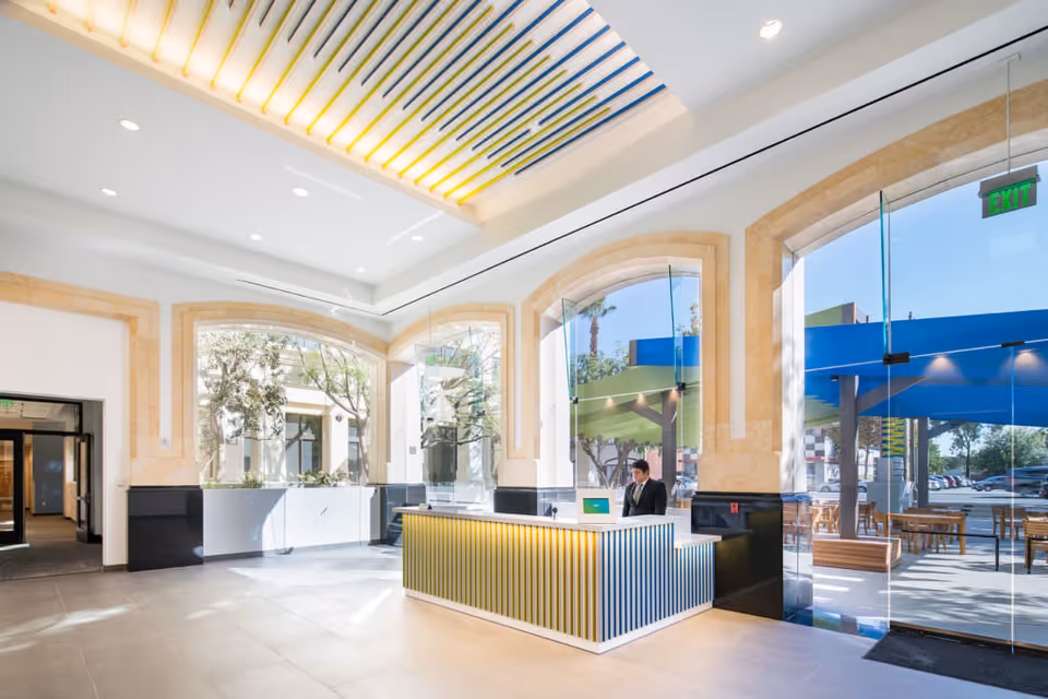 Bright modern lobby with a striped reception desk, large arched windows, and outdoor seating.