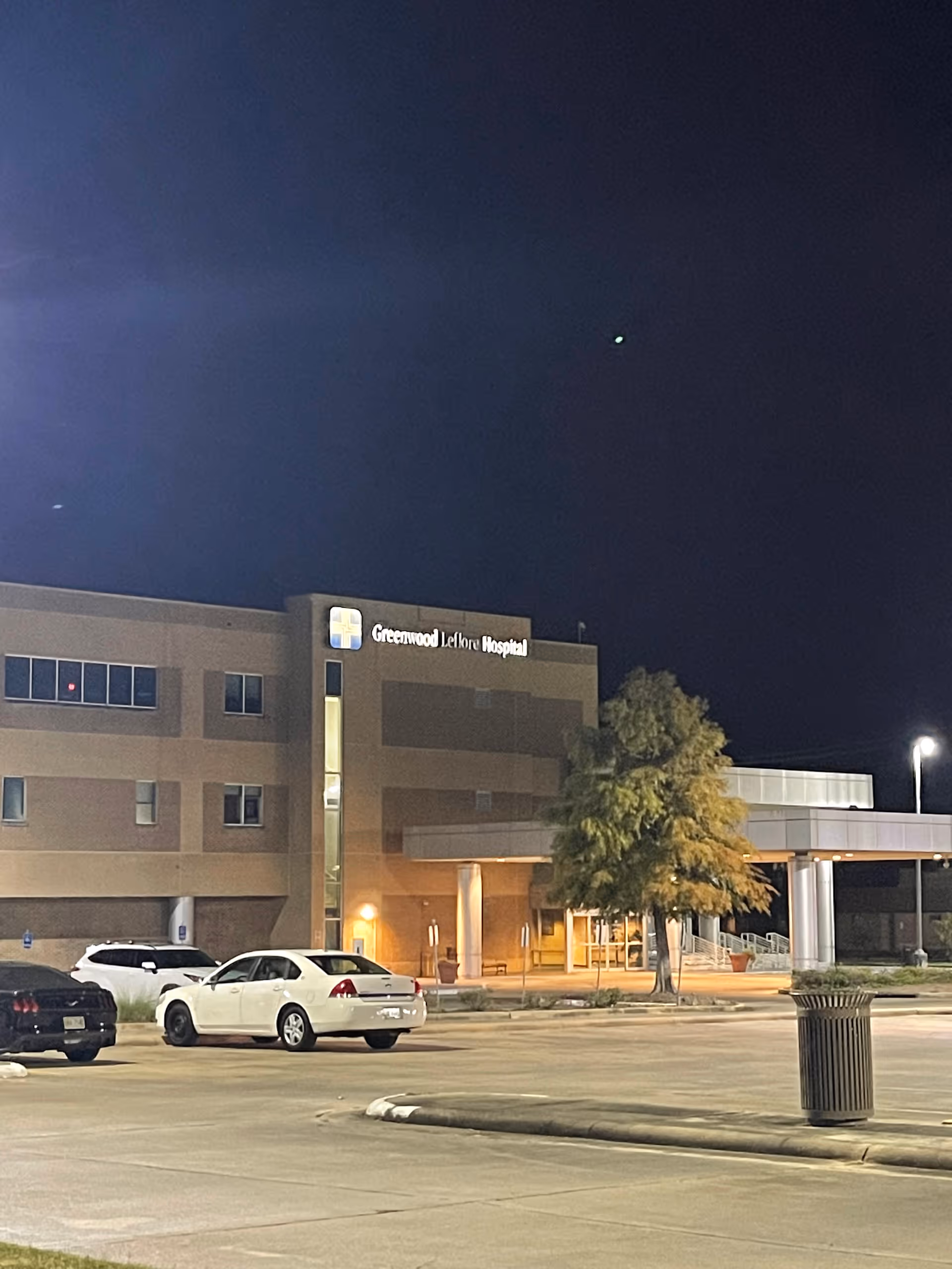 Night view of Greenwood Leflore Hospital entrance with parked cars in front.