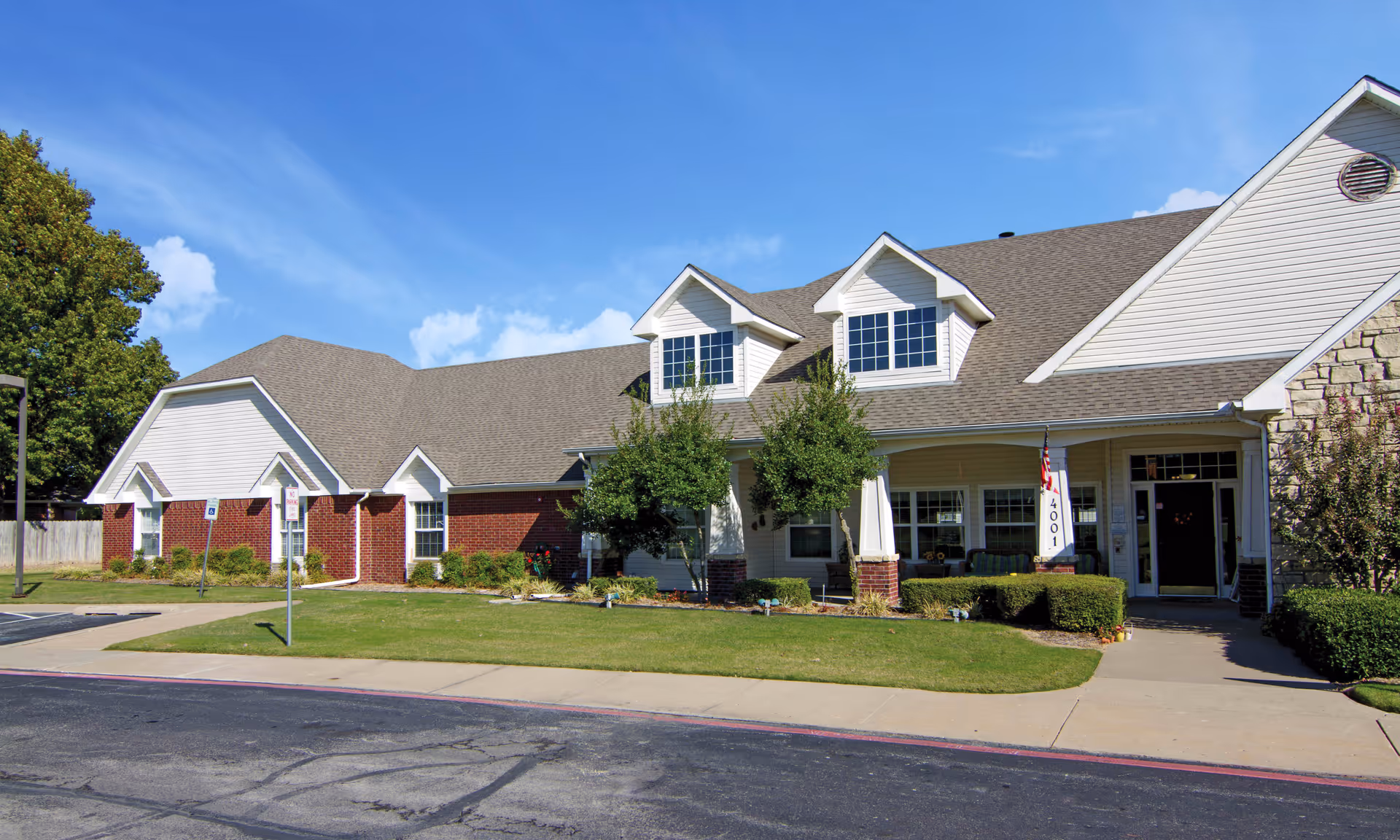 Exterior view of Brookdale Broken Arrow facility with a welcoming entrance, manicured lawn, and blue sky.