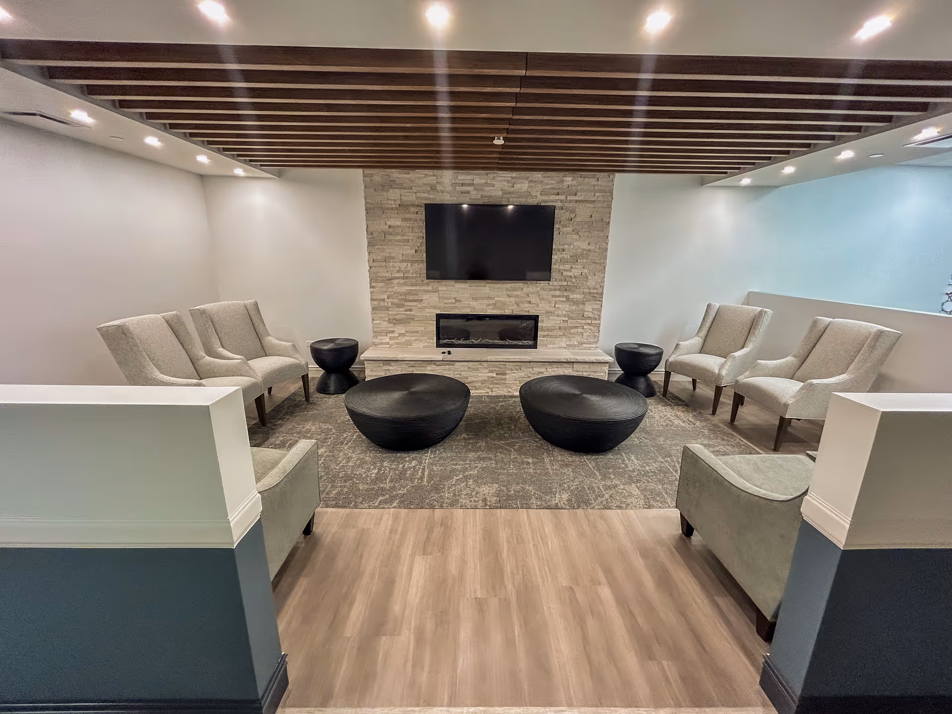 Modern lounge area with a stone fireplace, mounted TV, and circular coffee tables.