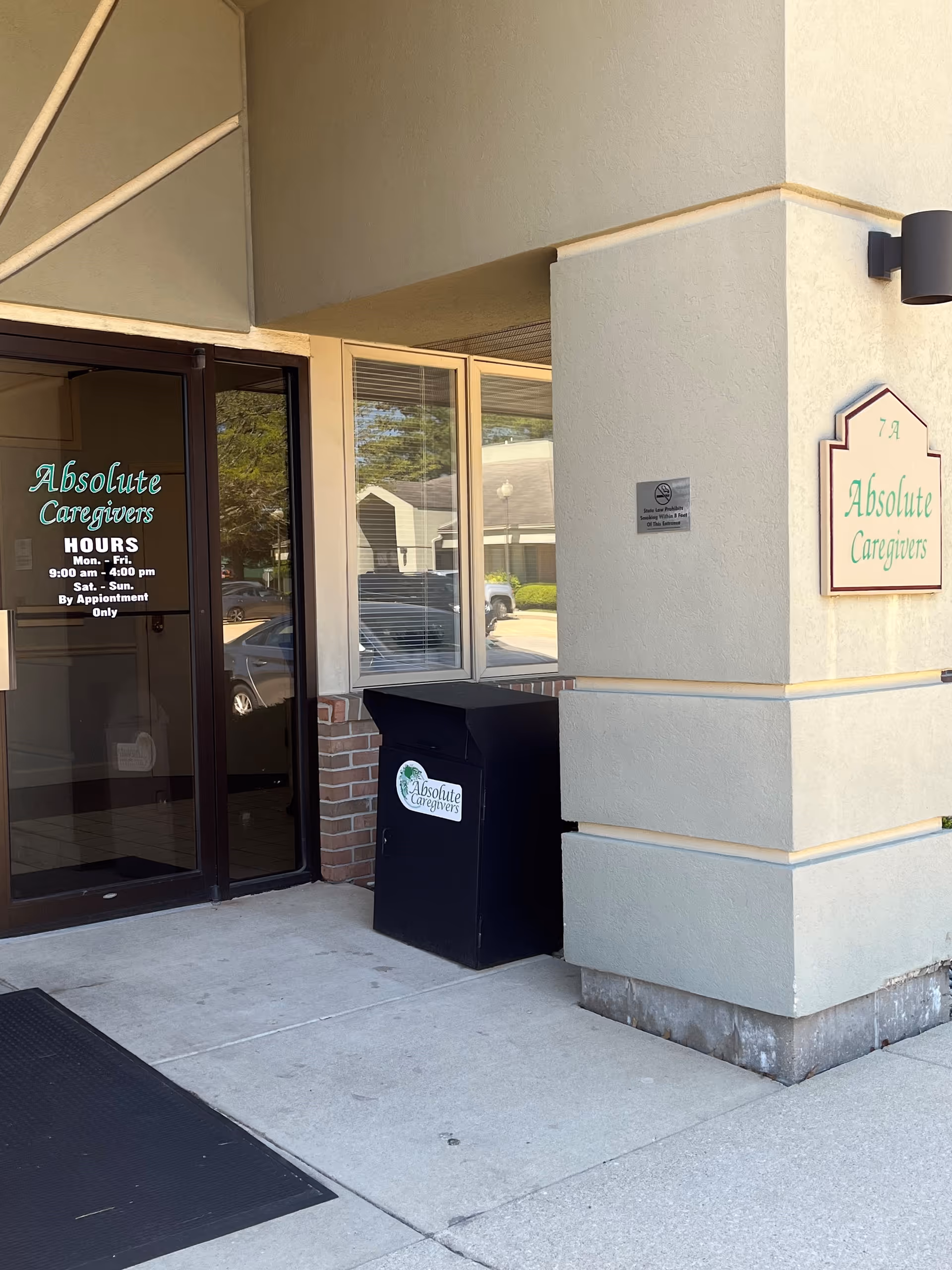 Exterior view of Absolute Caregivers entrance with glass door, sign, and black trash/recycling bin.