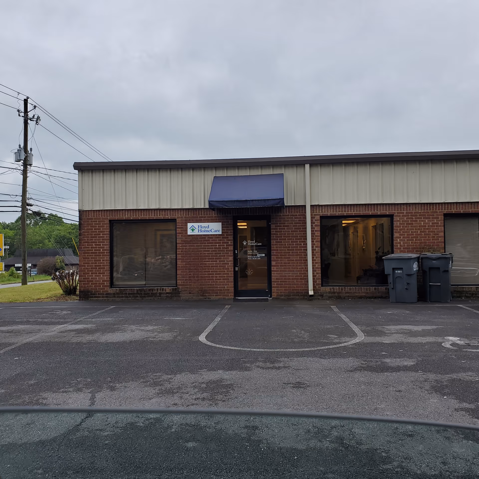 Brick storefront with a blue awning, Floyd HomeCare sign, and a parking lot in front.
