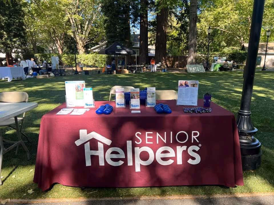 Outdoor park setup with a maroon Senior Helpers table and tents in background.