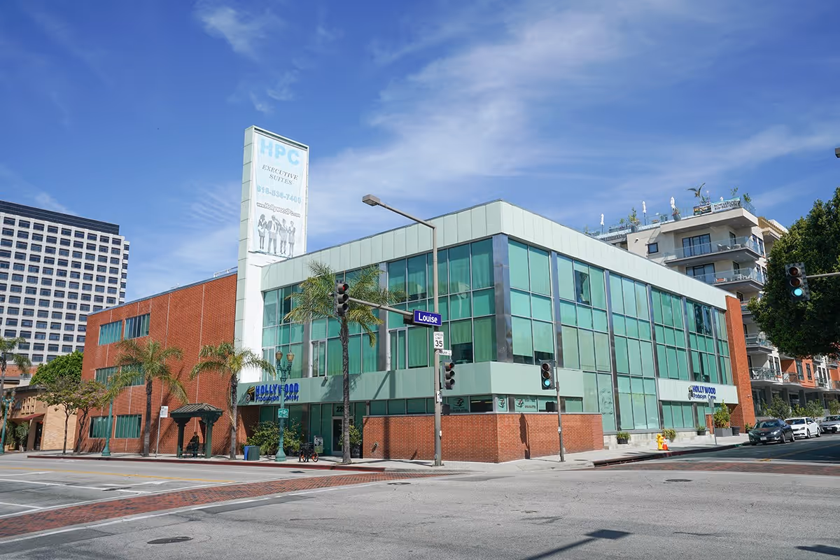 Modern glass-front senior care building on a city street with palm trees.