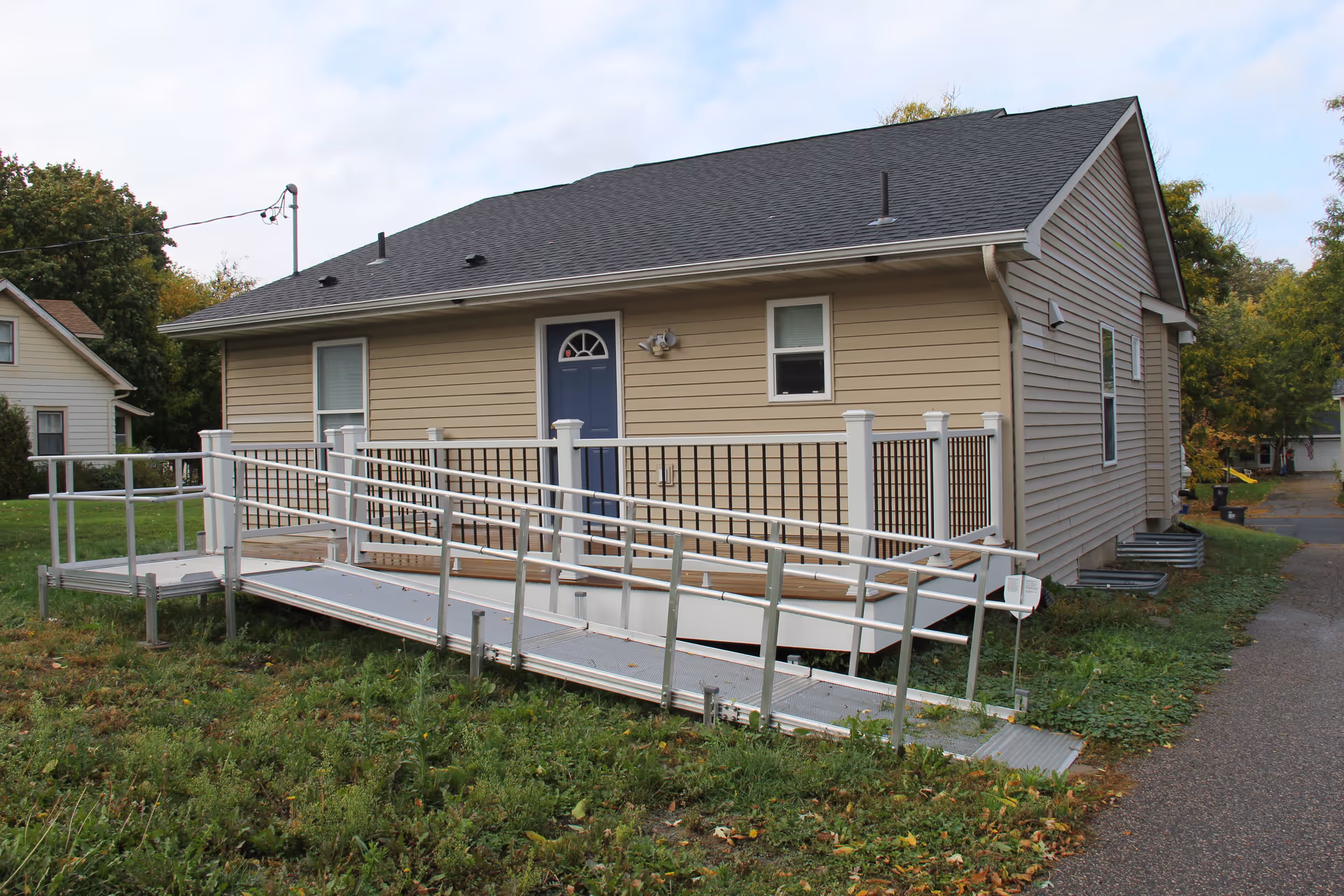 Single-story beige house with a blue front door and an exterior wheelchair ramp leading to the entrance.