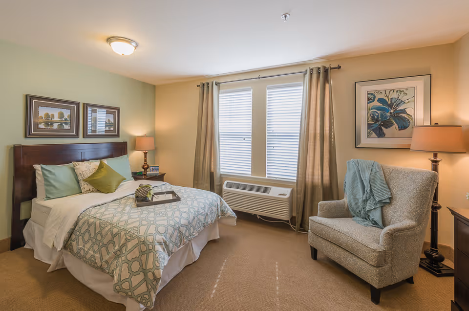 Cozy senior living bedroom with a bed, chair, lamps, and a window with curtains.