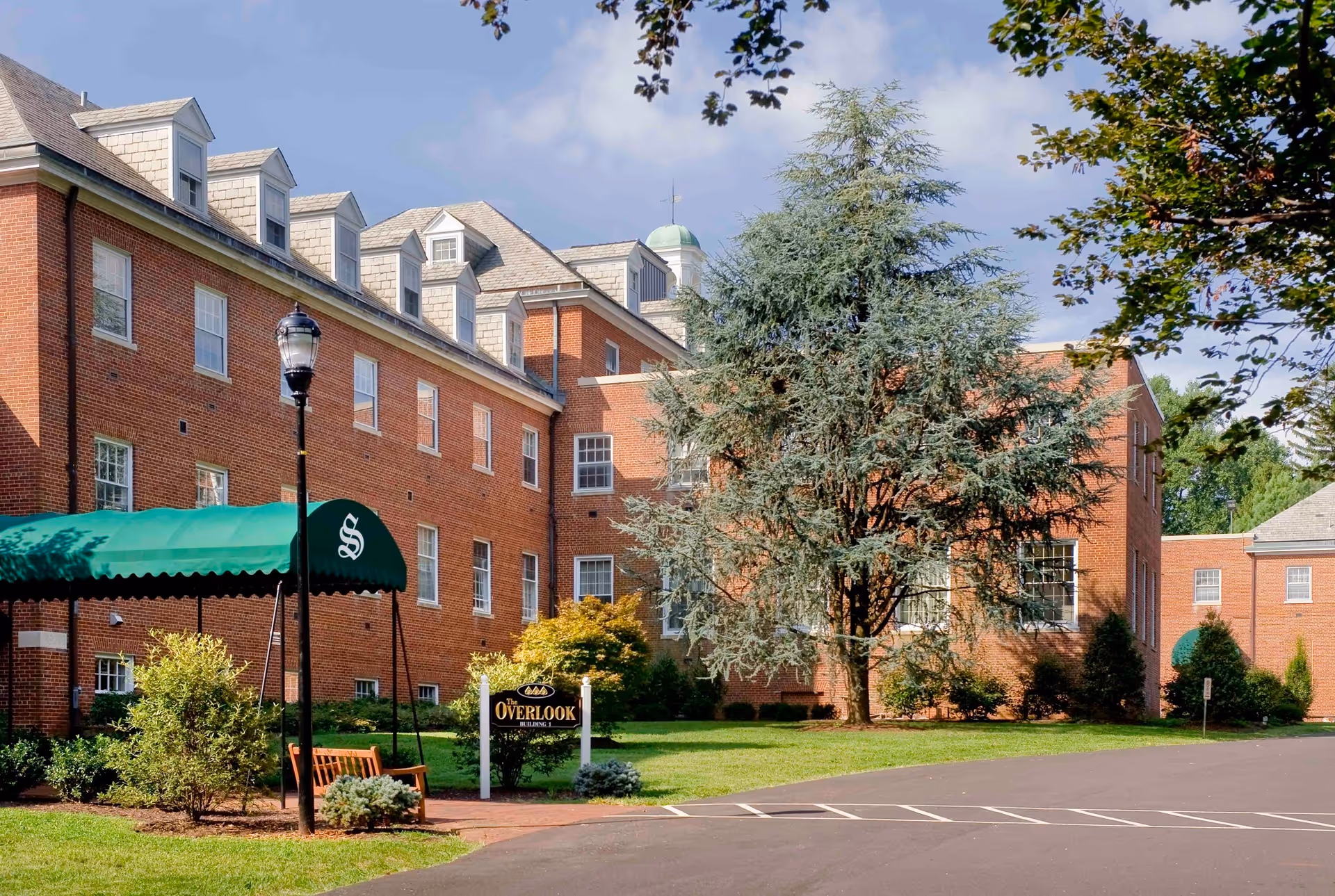 Brick senior living building with a green awning, lawn, trees, and Overlook sign at front