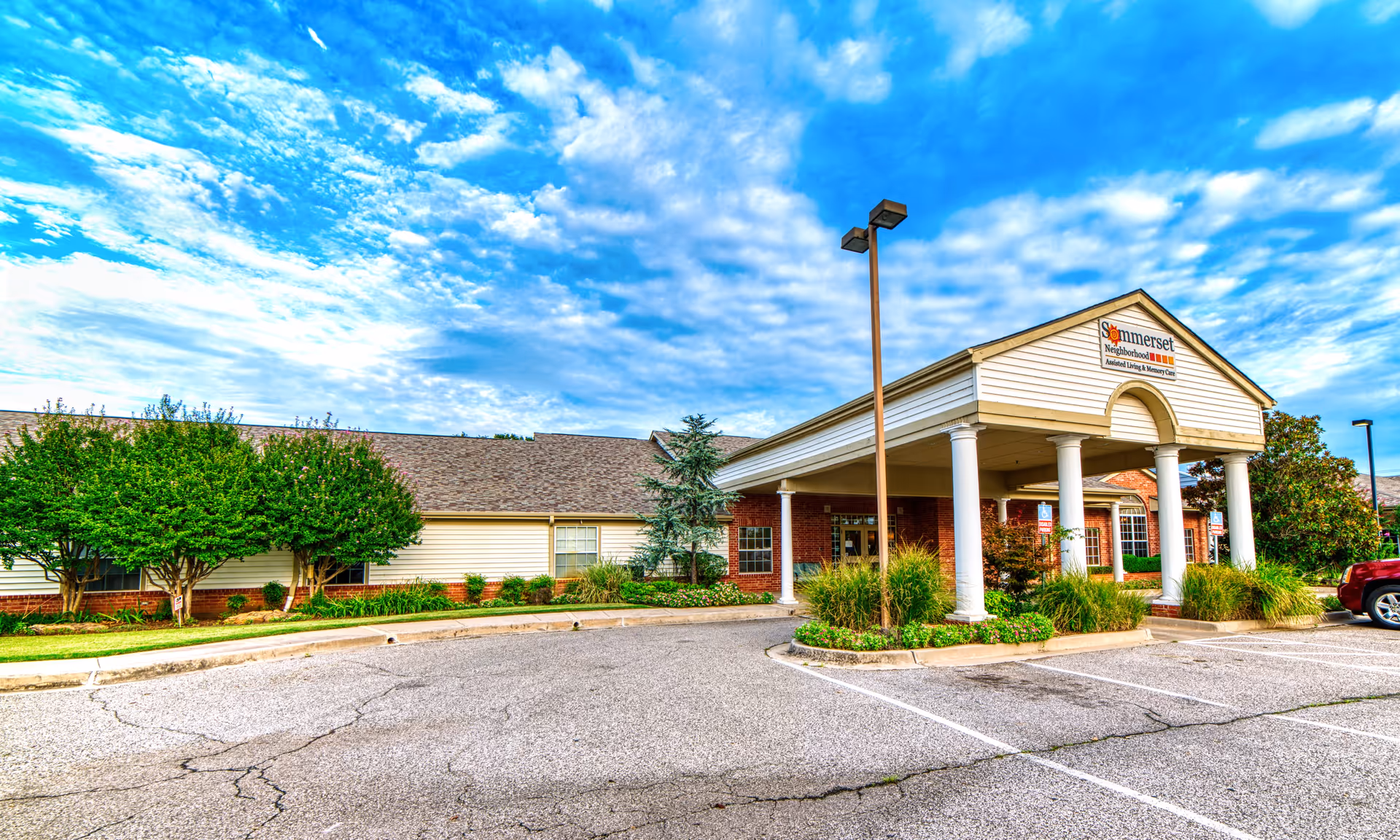 Exterior view of Somerset Neighborhood senior living facility with front entrance, parking lot, and landscaped grounds.