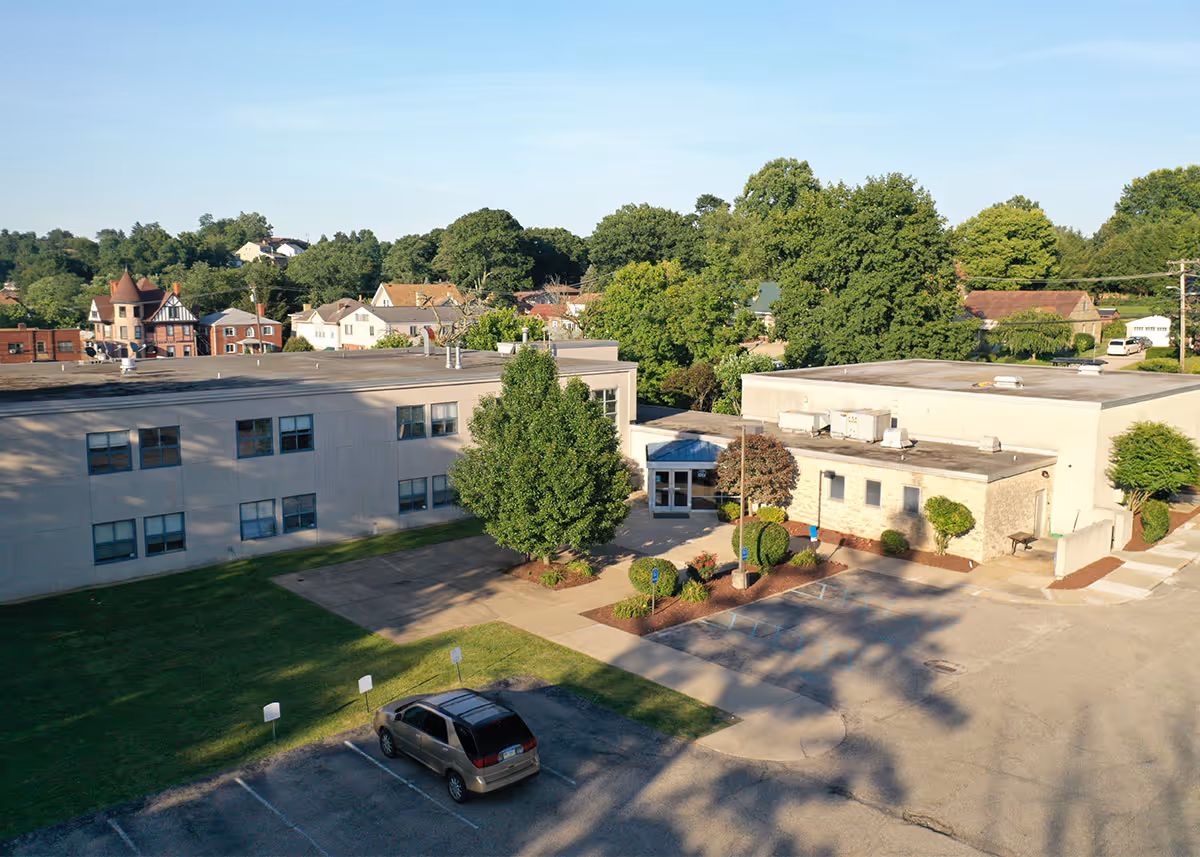 Aerial exterior view of a senior living campus with parking, trees, and low rise buildings.