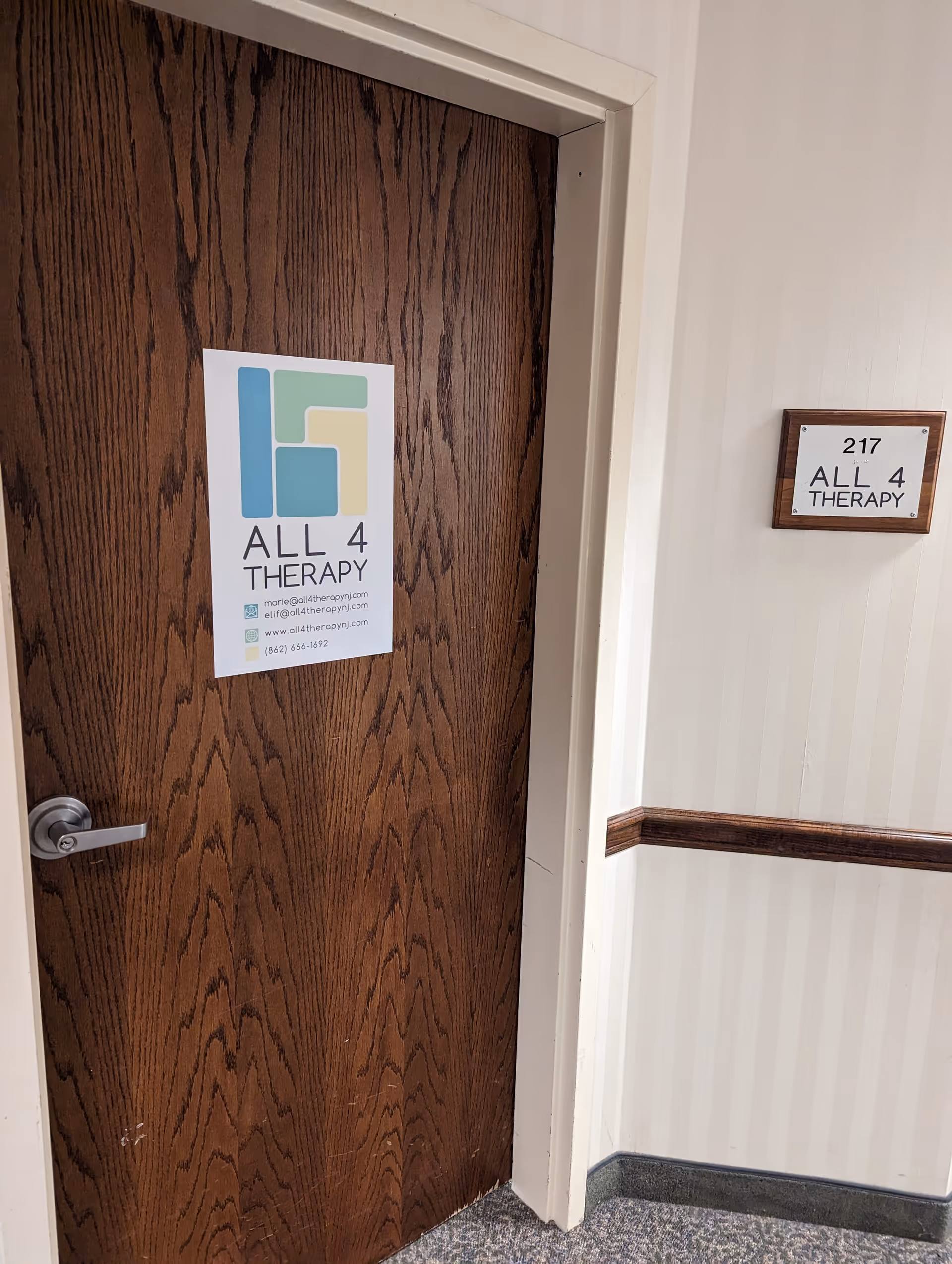 Wooden door with All 4 Therapy sign in a beige interior hallway.