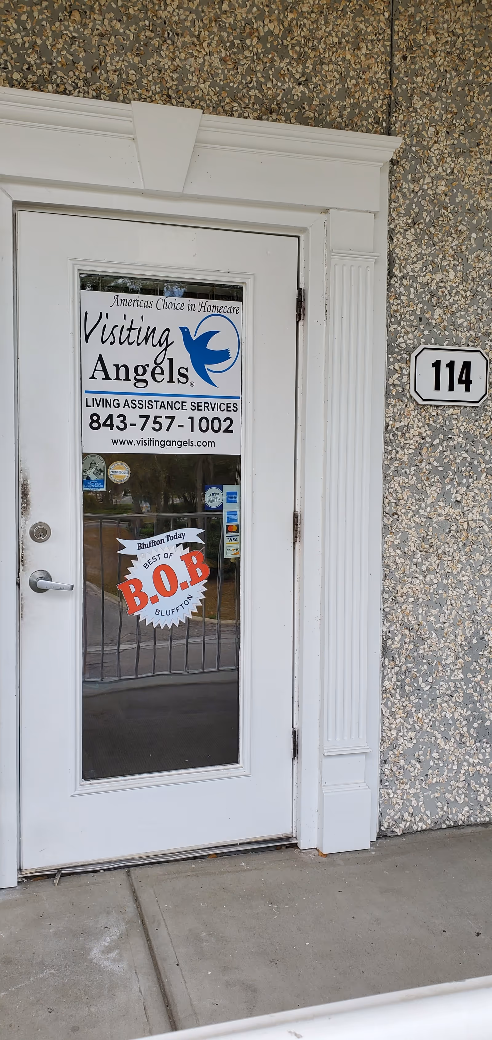 White exterior door with Visiting Angels sign and house number 114 on textured wall.