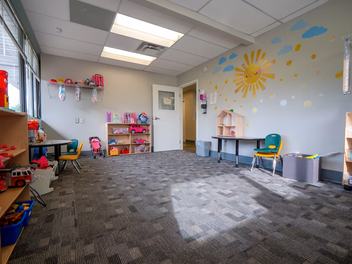 Bright playroom with toy shelves, small chairs, and a sun mural.