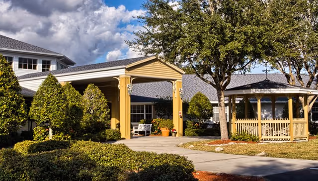 Front view of a senior living facility entrance with a gazebo and landscaped greenery.