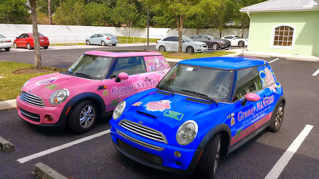 Two colorful Granny Nannies branded cars parked in a lot beside a green building.