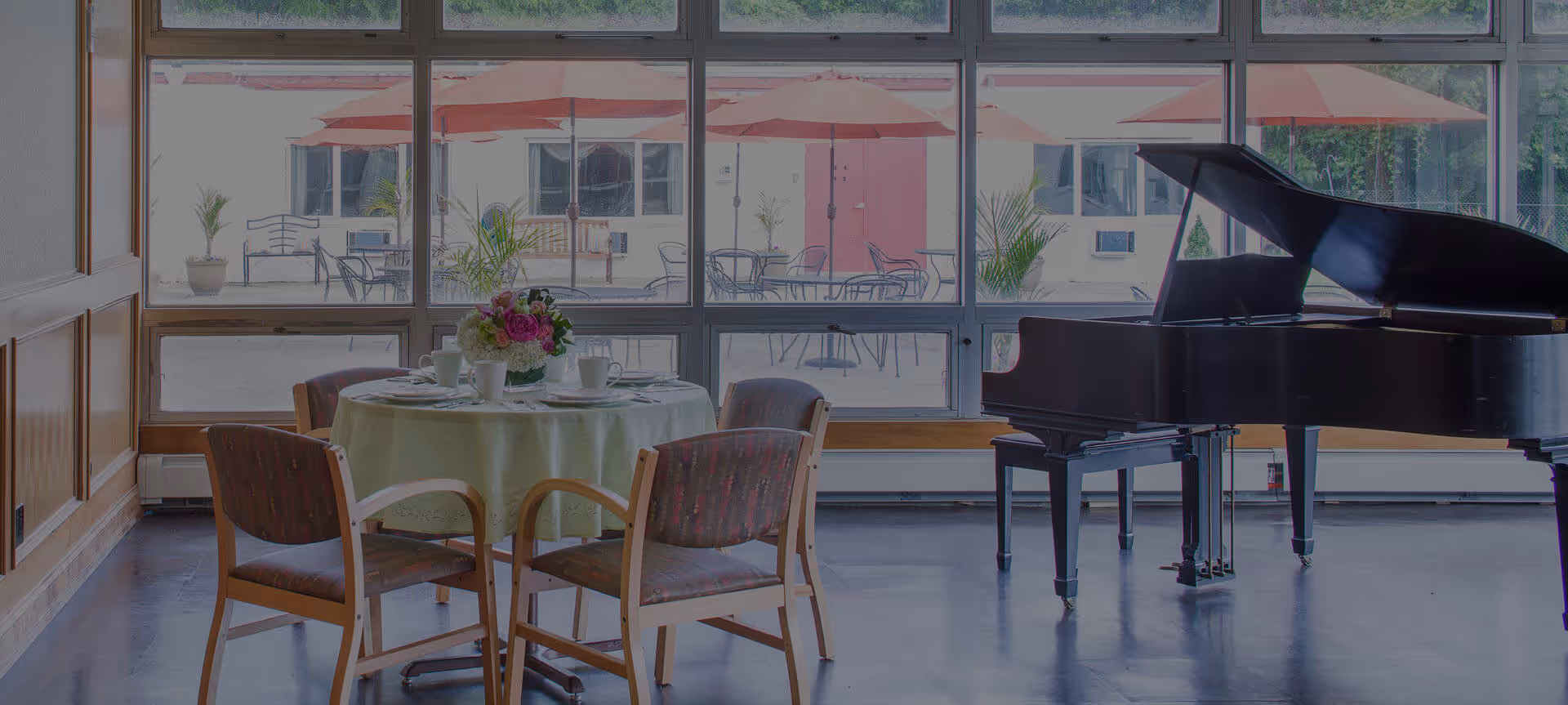 A bright interior common area with a round dining table set for dining and a grand piano.