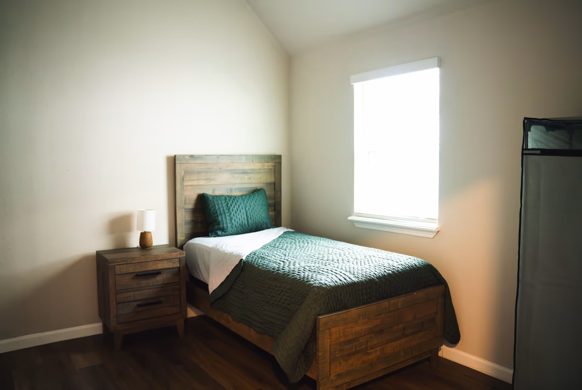 A small bedroom with a wooden single bed, nightstand, and window.