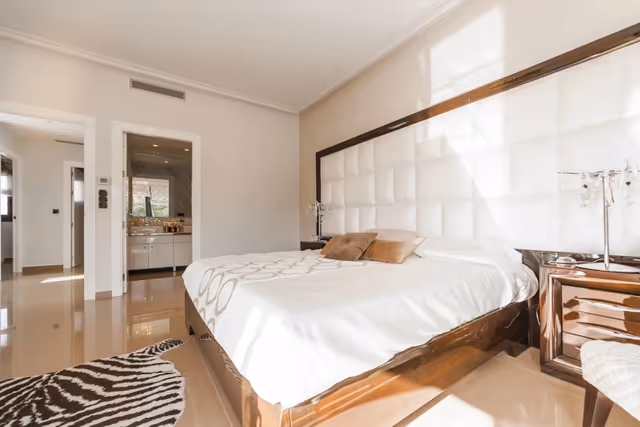 Bright bedroom with a large bed, padded headboard, nightstands, and a zebra rug.
