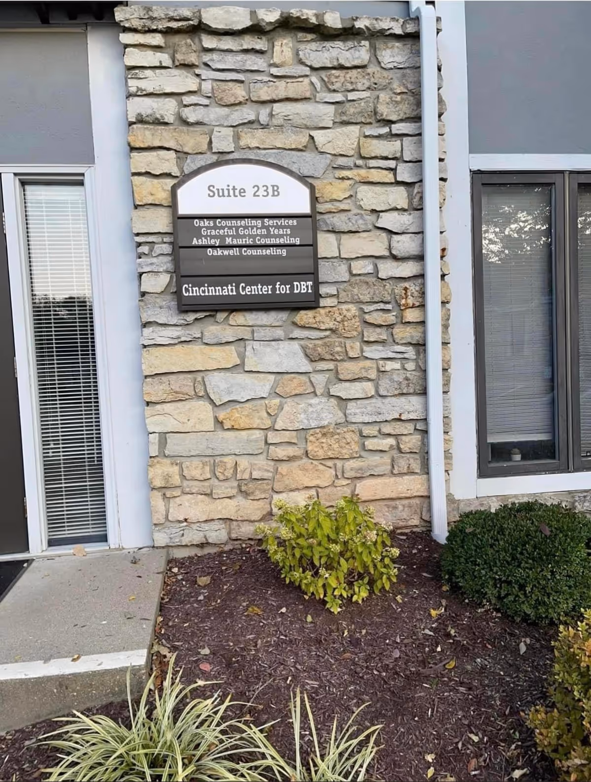 Stone building entrance with Suite 23B sign and landscaping