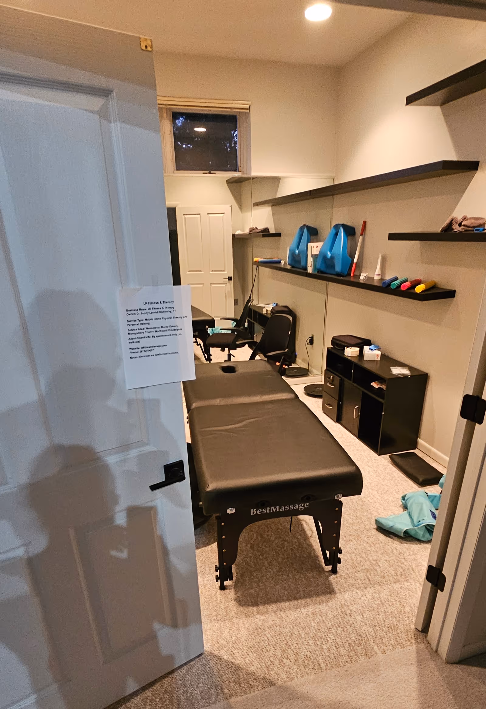 Therapy room with a massage table, chairs, and shelving in LK Fitness & Therapy.