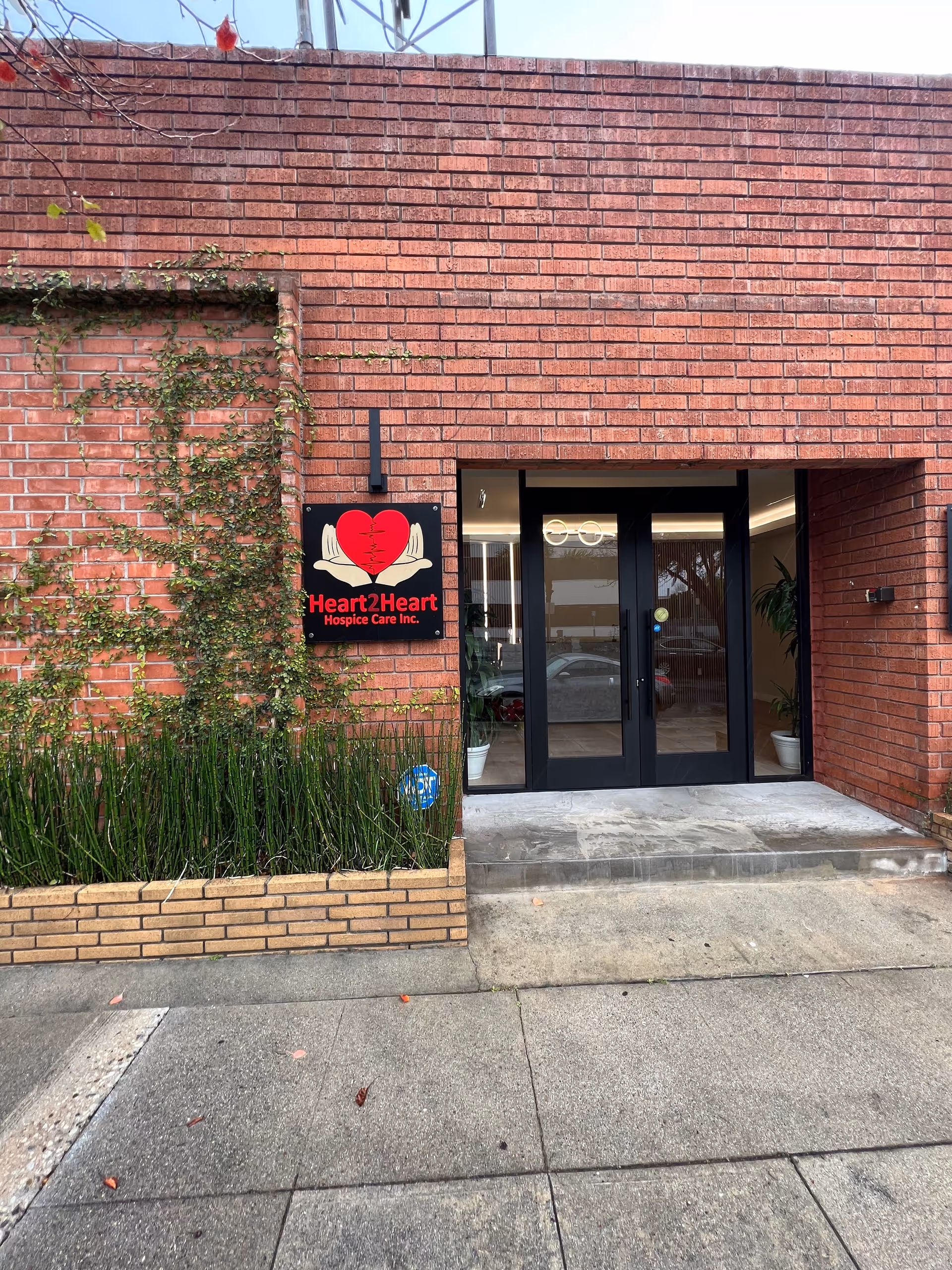 Brick building entrance with glass doors and a Heart2Heart Hospice sign.