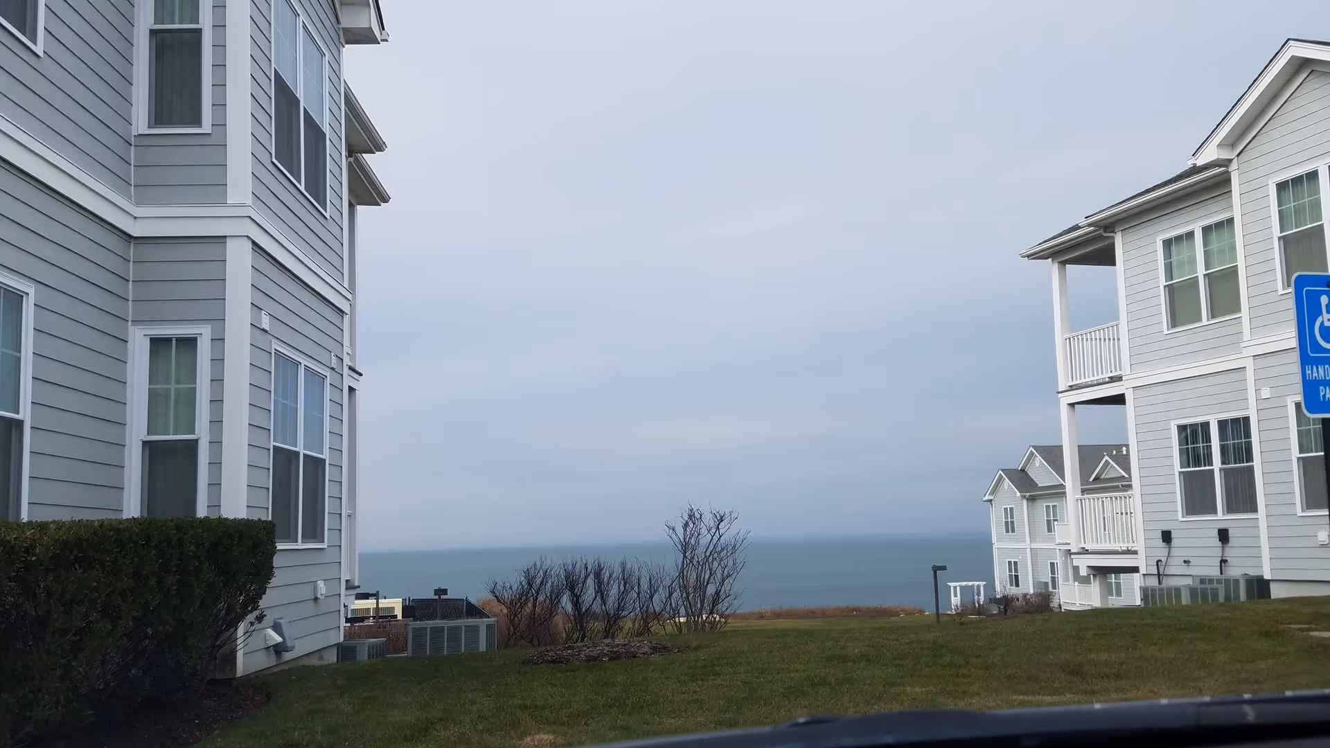 Two light-gray residential buildings overlook a grassy lawn toward the ocean.