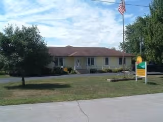 Front exterior of a single-story Sunnyhills Residential Care Facility with sign and flag.