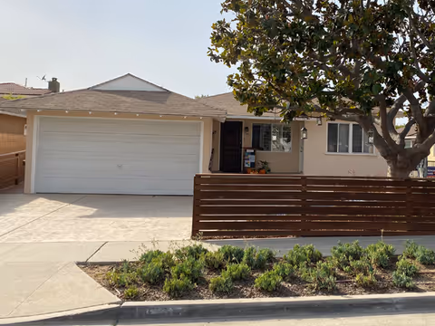 Single-story memory care facility front with garage, fence, and tree.