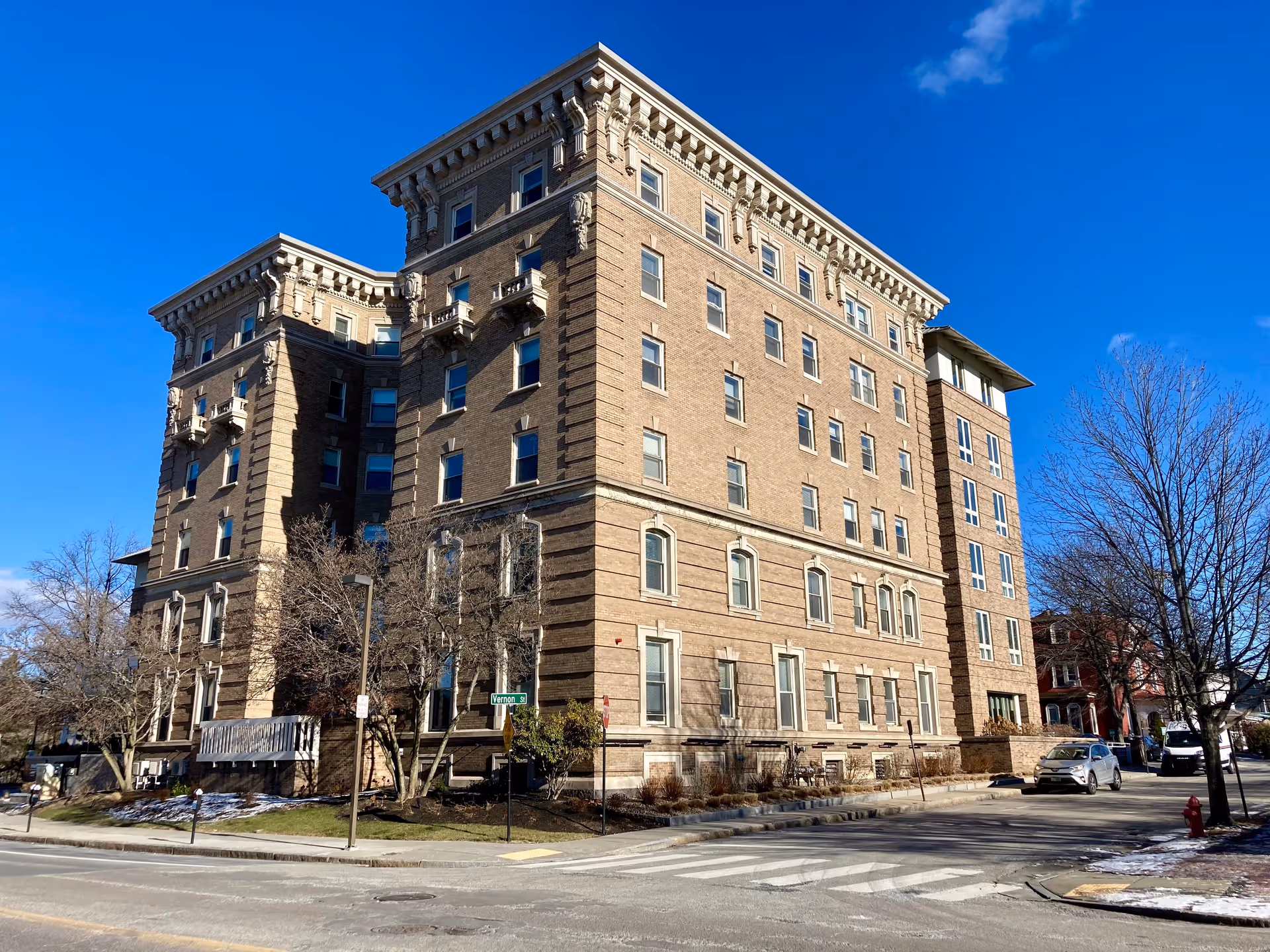 Large multi-story brick residential building on a street corner under a clear blue sky.
