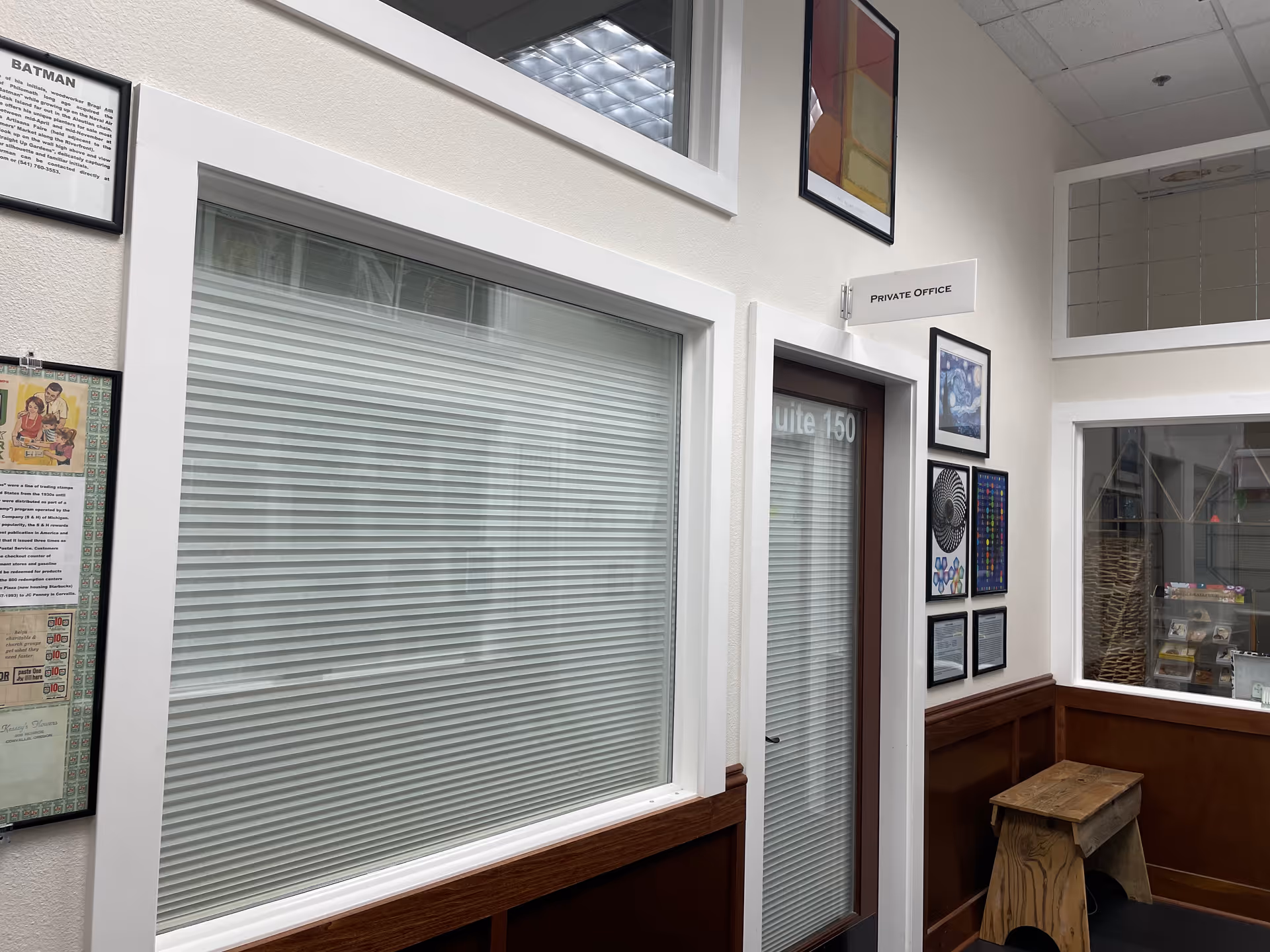 Interior hallway of a senior facility with large window blinds, framed art, and a private office.