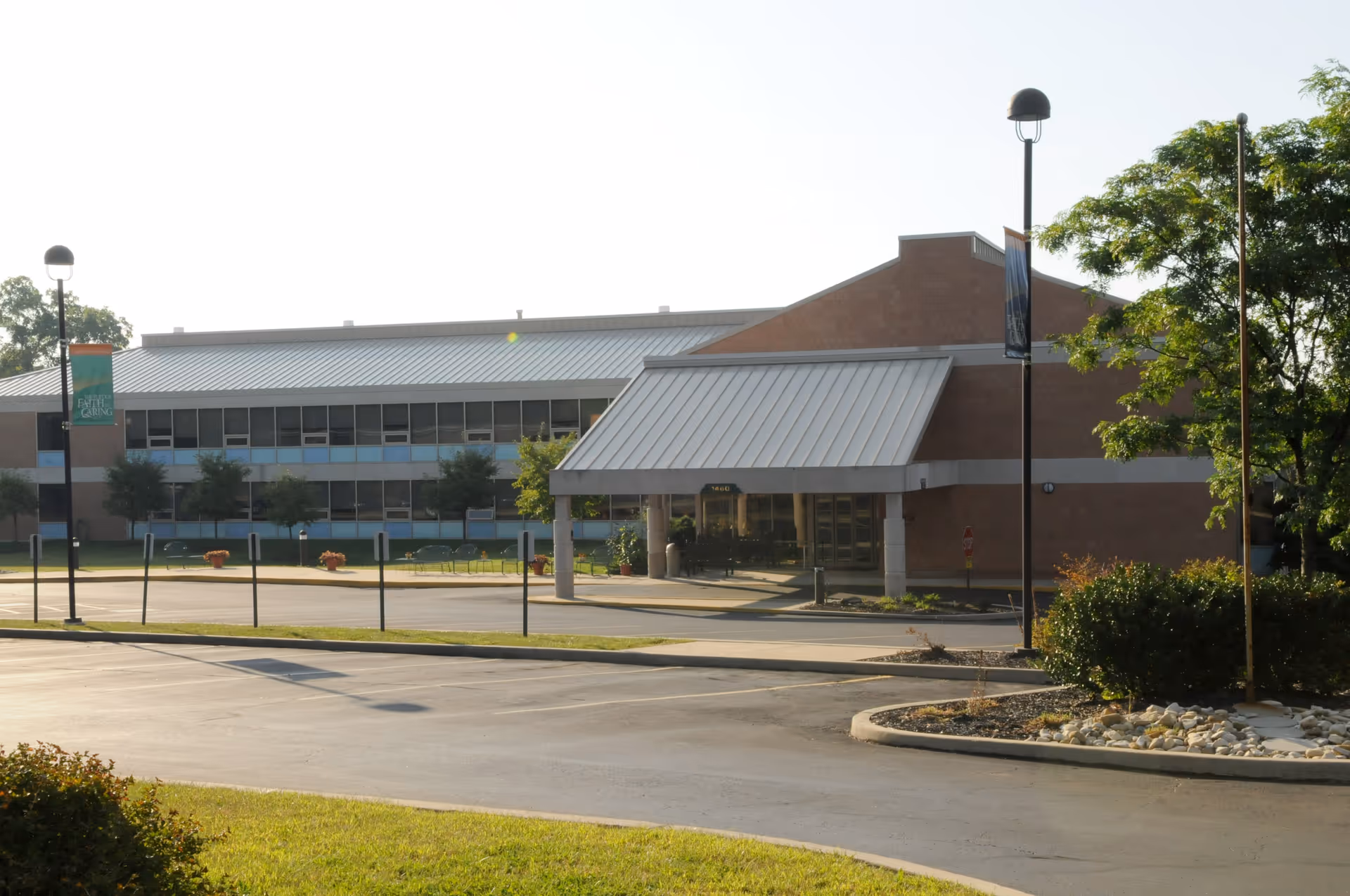 Front exterior of a two-story senior living facility with a covered entrance, driveway, and landscaped grounds.