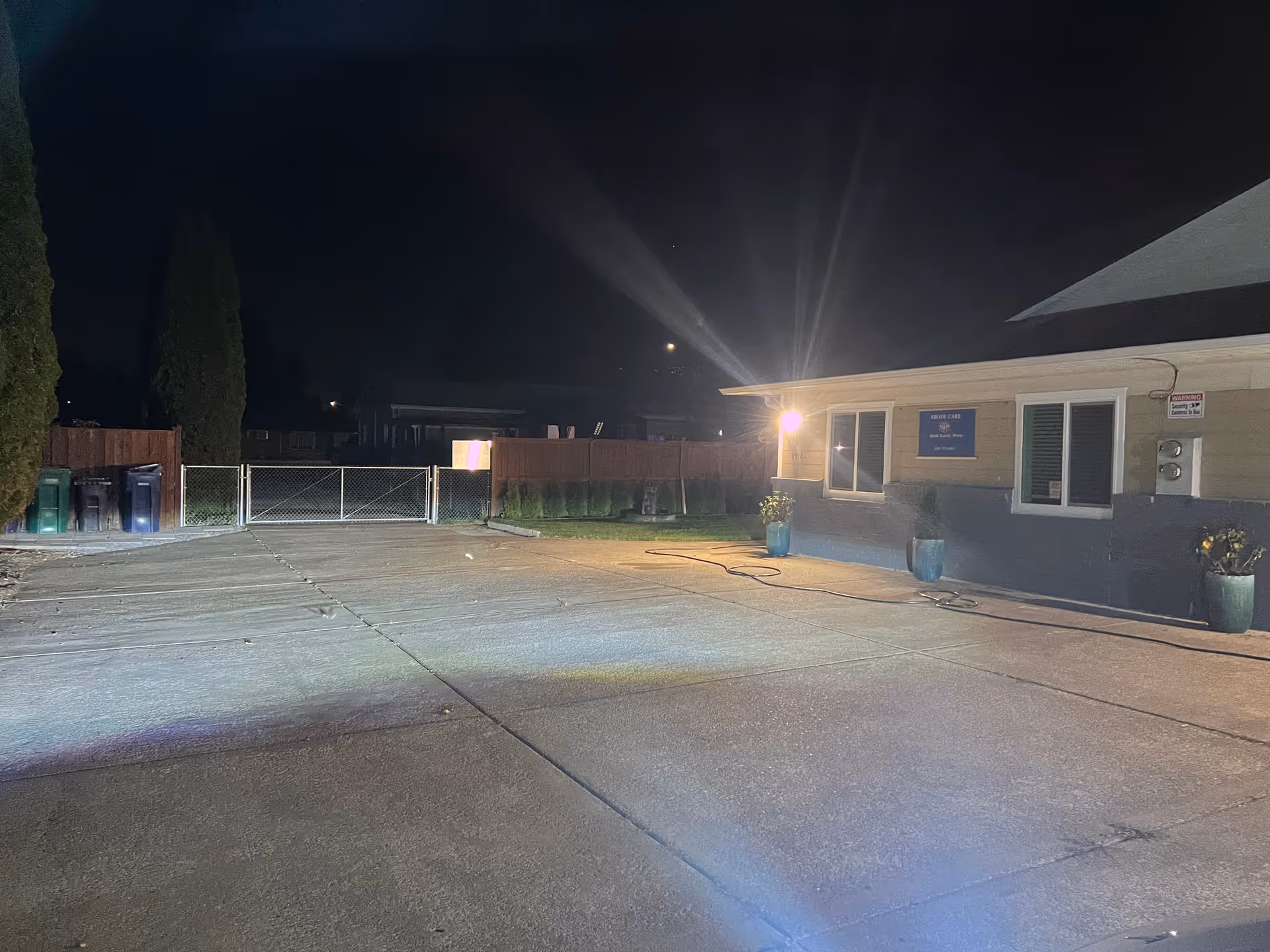 Night exterior of Abode Care AFH facility with gate, driveway, and front entrance.