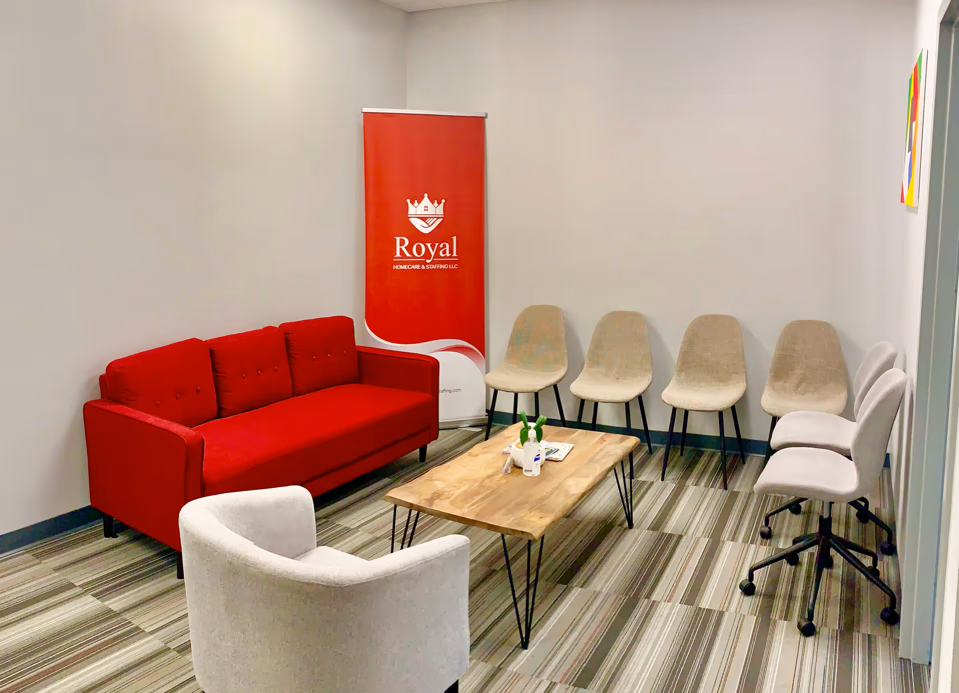 A waiting room with a red sofa, beige chairs, a wooden coffee table, and Royal banner.