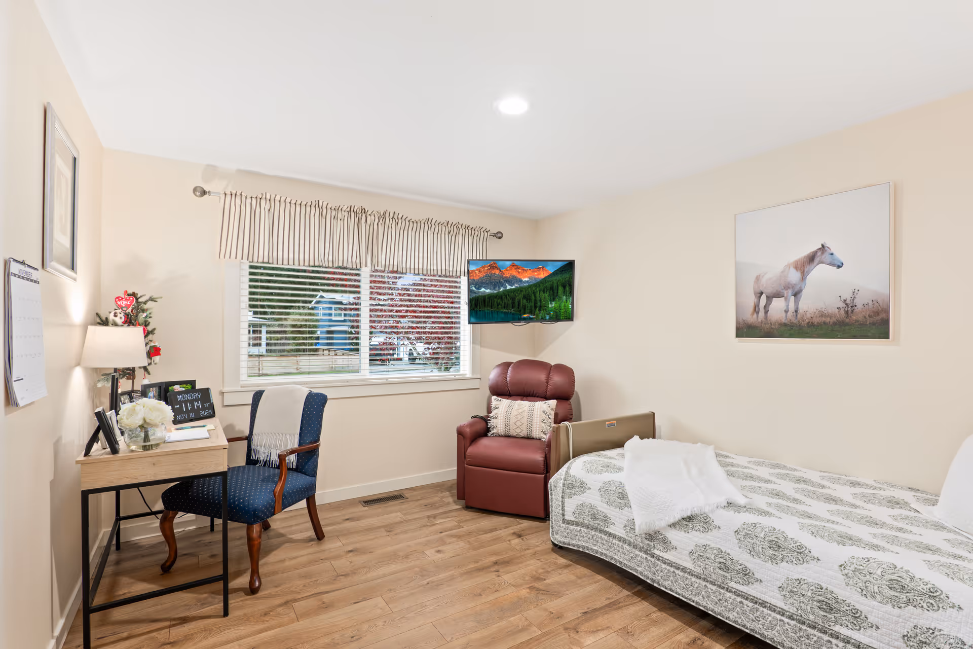 Bright bedroom with bed, desk, blue chair, recliner, window, wall art.