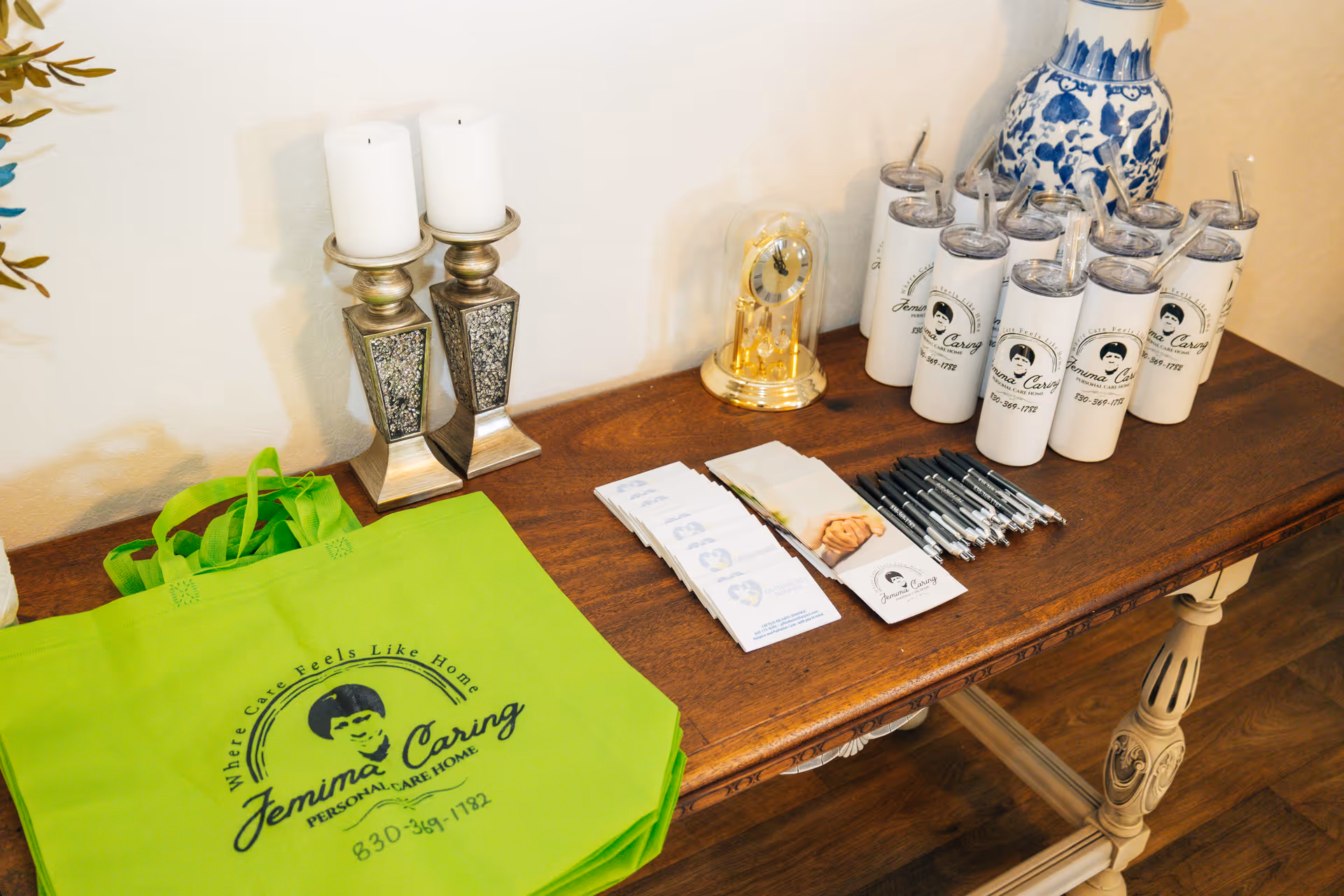 Promotional table featuring Jemina Caring Personal Care Home items, brochures, pens, and branded bottles.