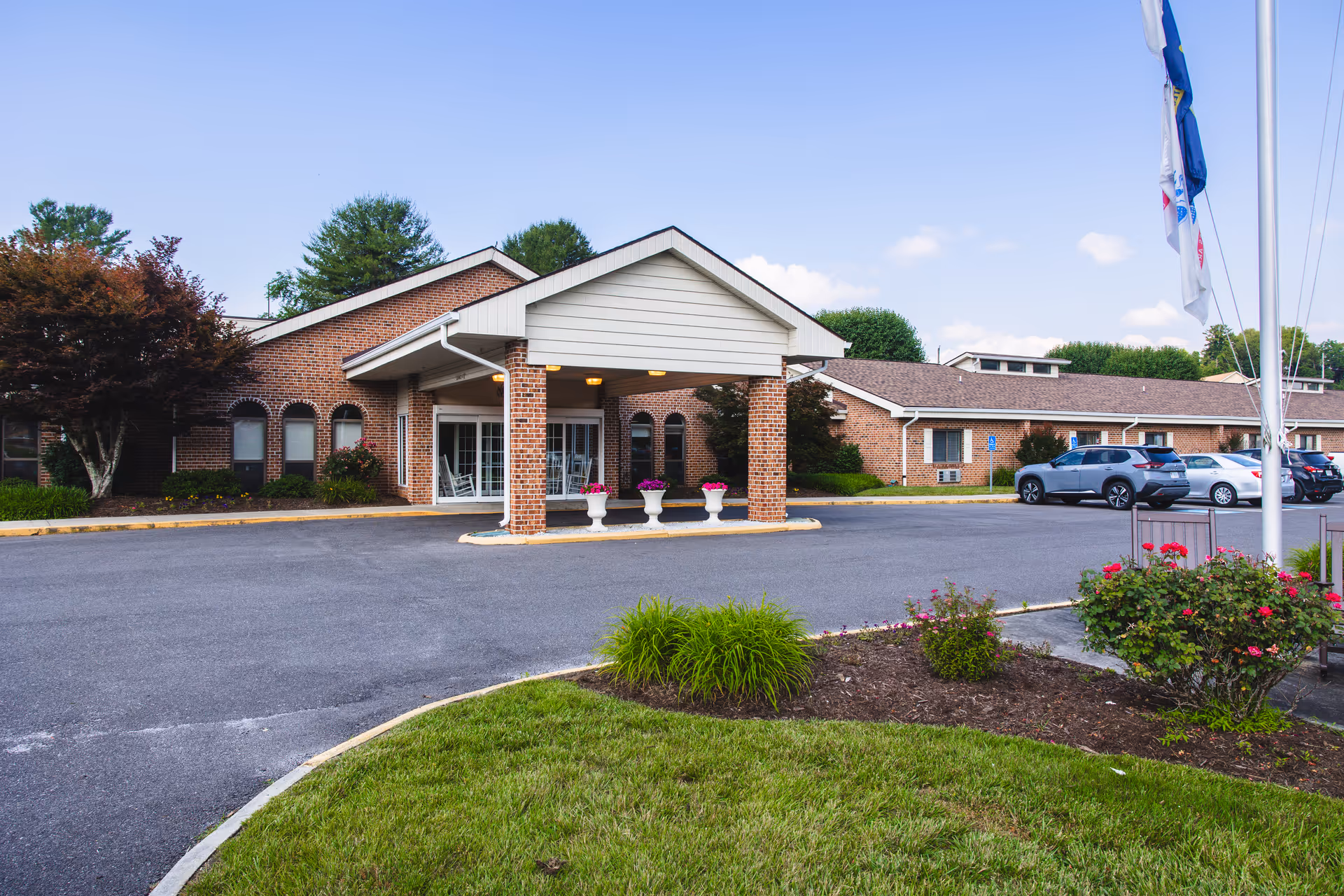 Brick senior living facility with covered entrance, parking lot, flags, and landscaping.