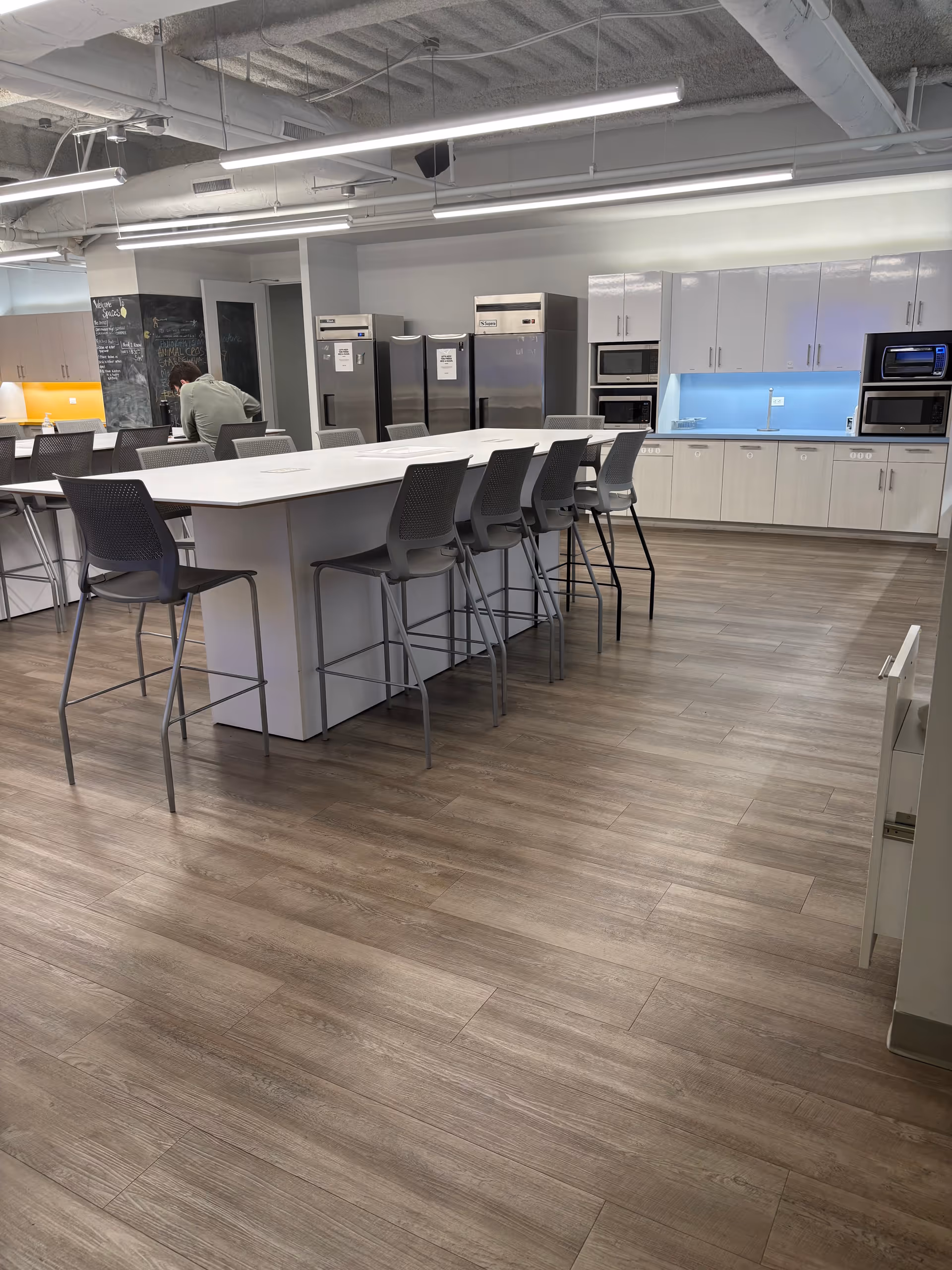 A modern communal kitchen area with a long island, bar stools, and stainless appliances.