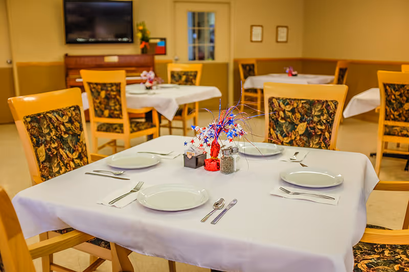 Dining room with tables covered in white tablecloths set with plates and utensils and a red, white, and blue star centerpiece.
