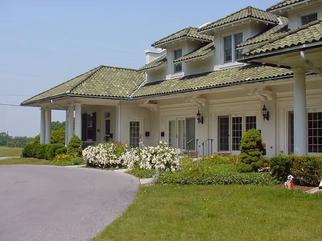 Exterior view of Hill Farm Estate featuring a white building with a green tiled roof, surrounded by landscaped gardens and flowers.